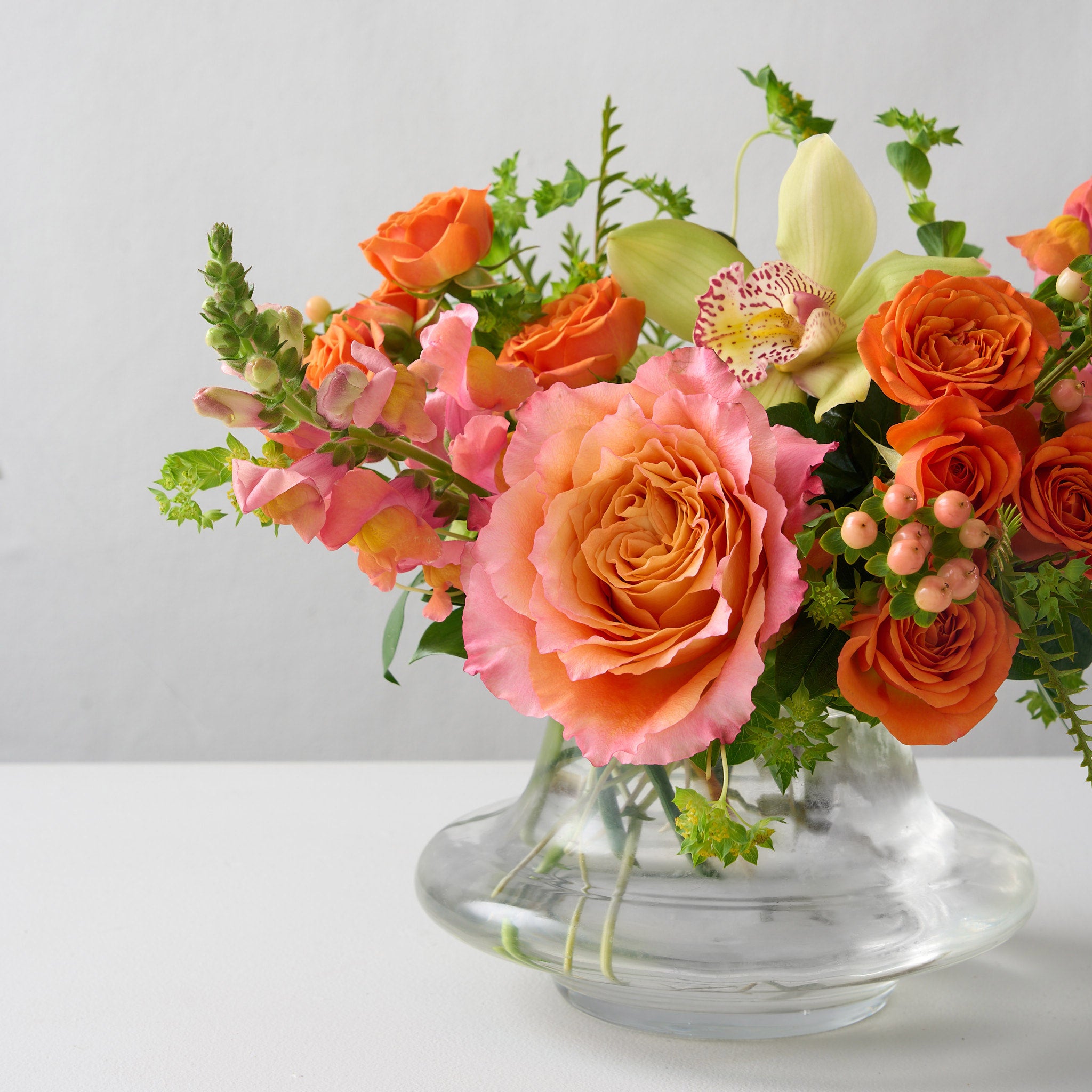 ellie flower arrangement in clear glass vase with orange spray roses, peach snapdragons, green cymbidium orchid and Bupleurum