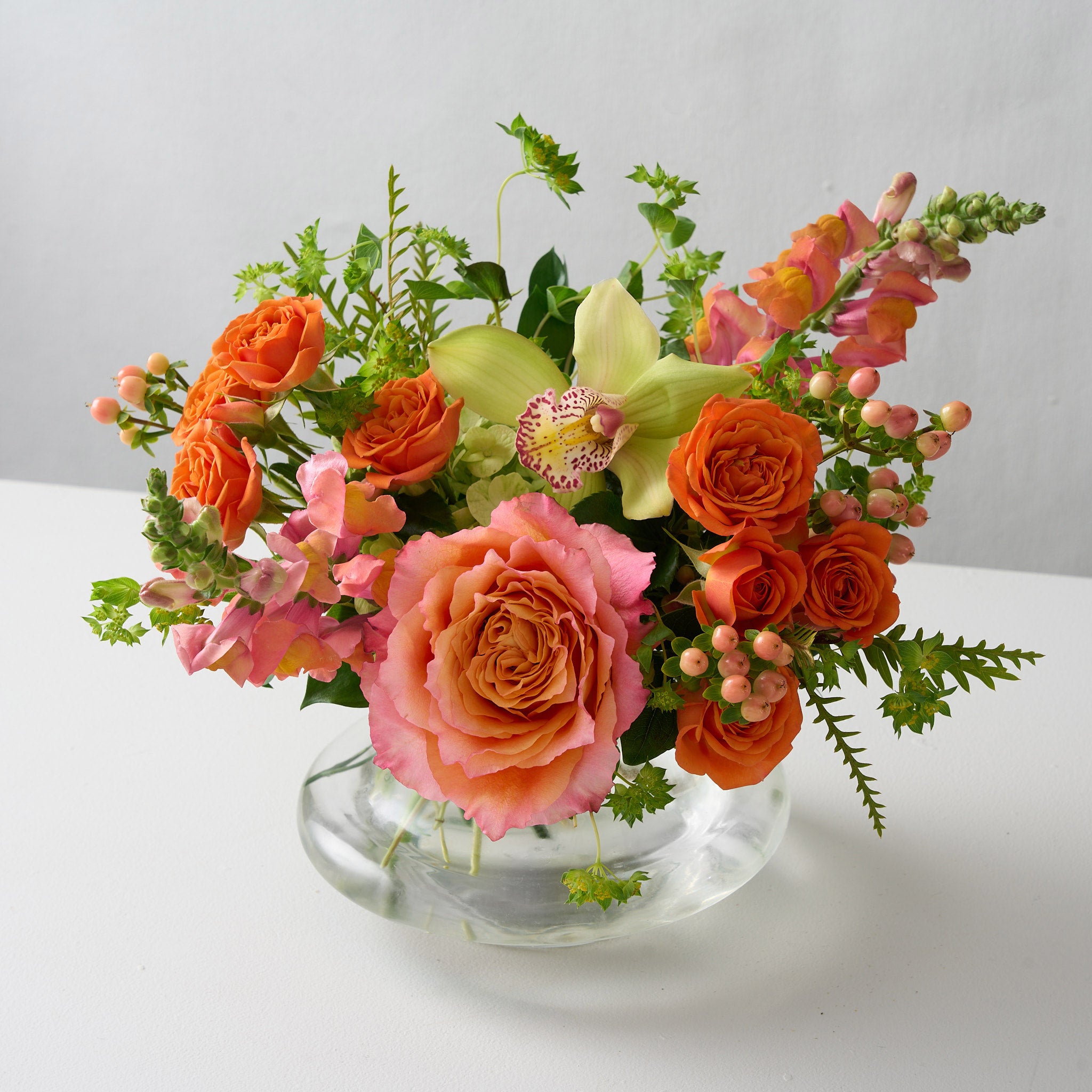 ellie flower arrangement  in clear glass vase with orange spray roses, peach snapdragons, green cymbidium orchid and Bupleurum