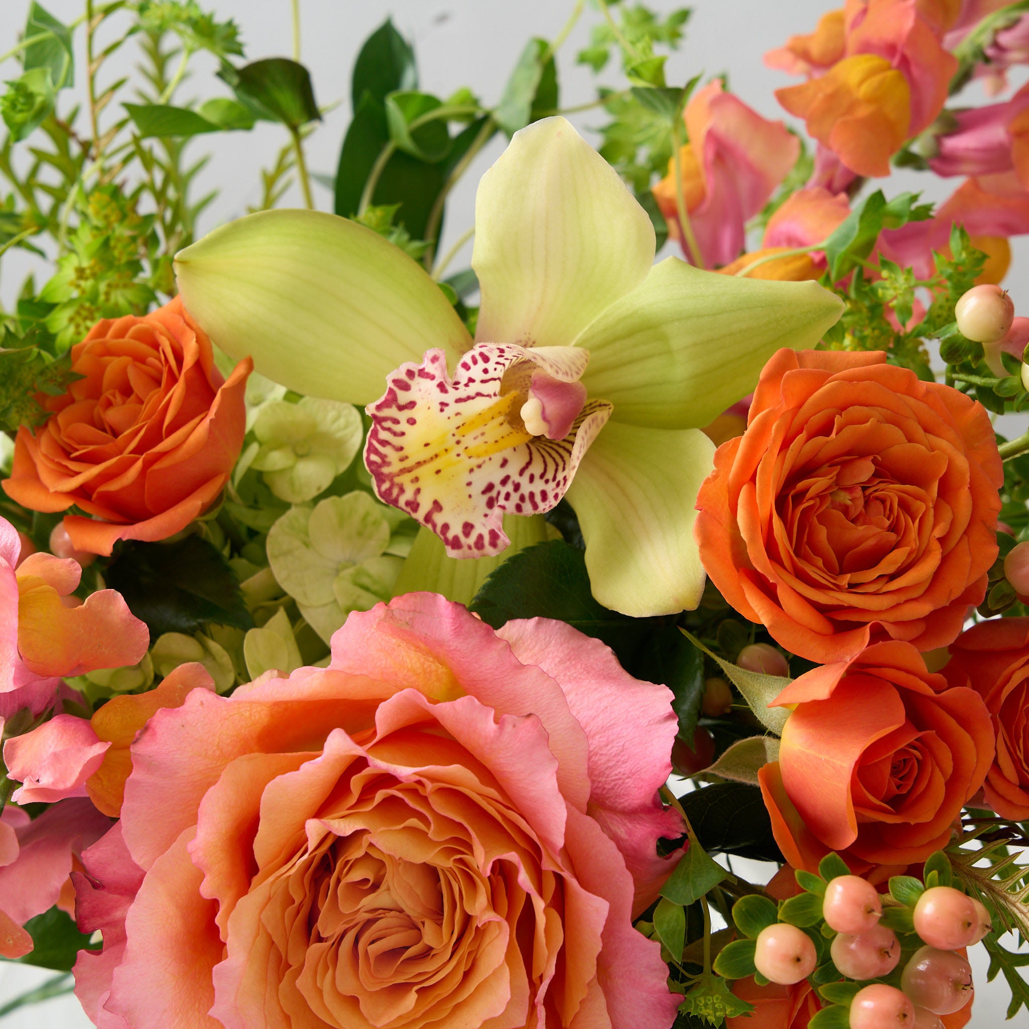 ellie flower arrangement in clear glass vase with orange spray roses, peach snapdragons, green cymbidium orchid and Bupleurum