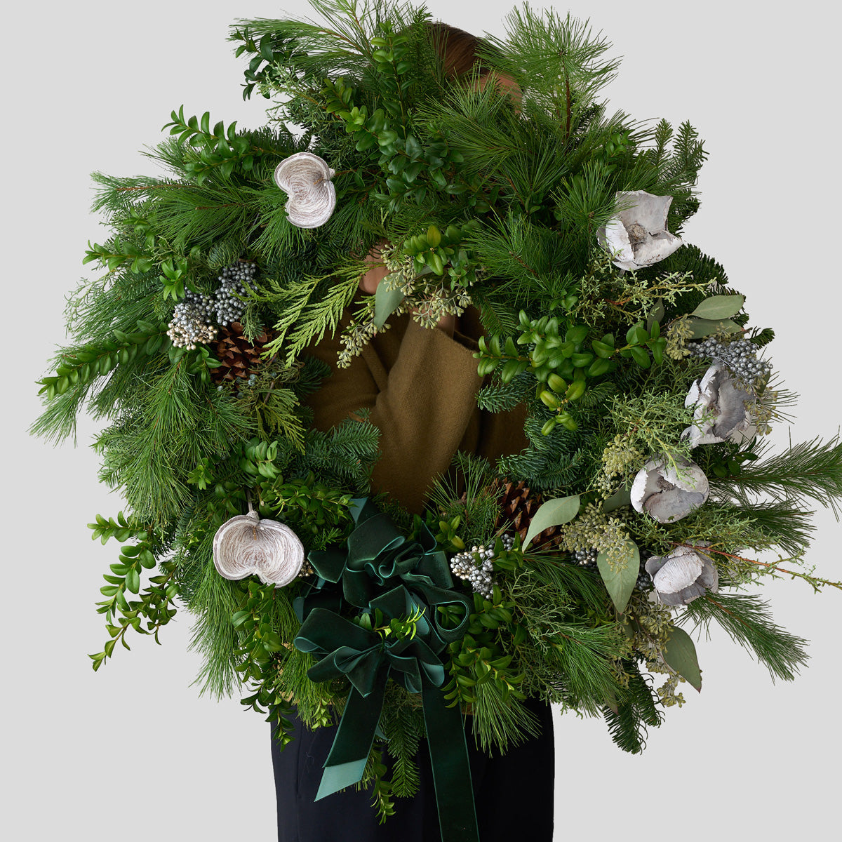 winter green Christmas wreath with silver badman pods, seeded eucalyptus, boxwood, fir, and pine branches with an emerald green bow.