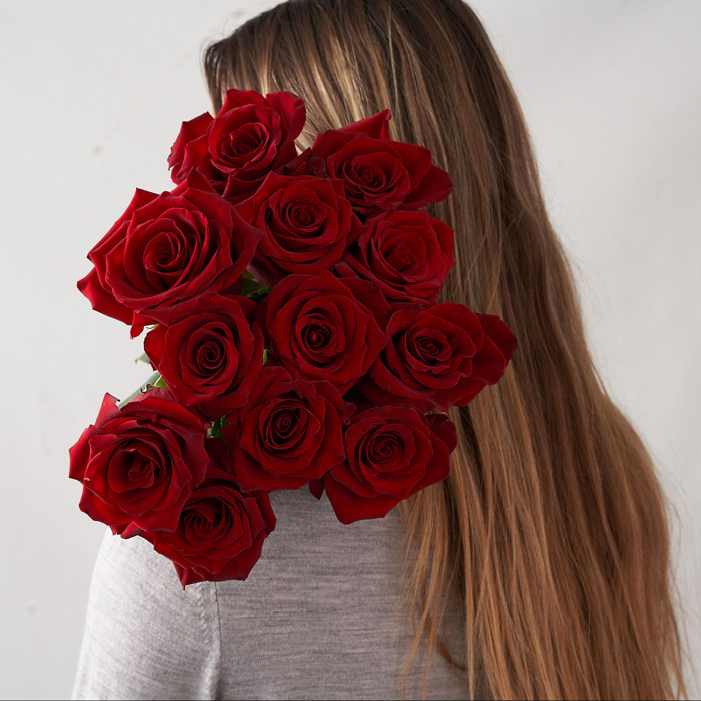 Woman holding a dozen red roses behind her back