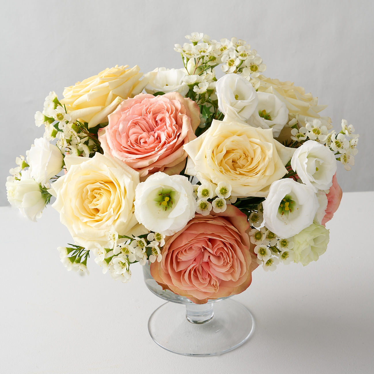 pink khala  and creamy  white candlelight roses, white wax flowers and lisanthus in a pedestal glass vase.