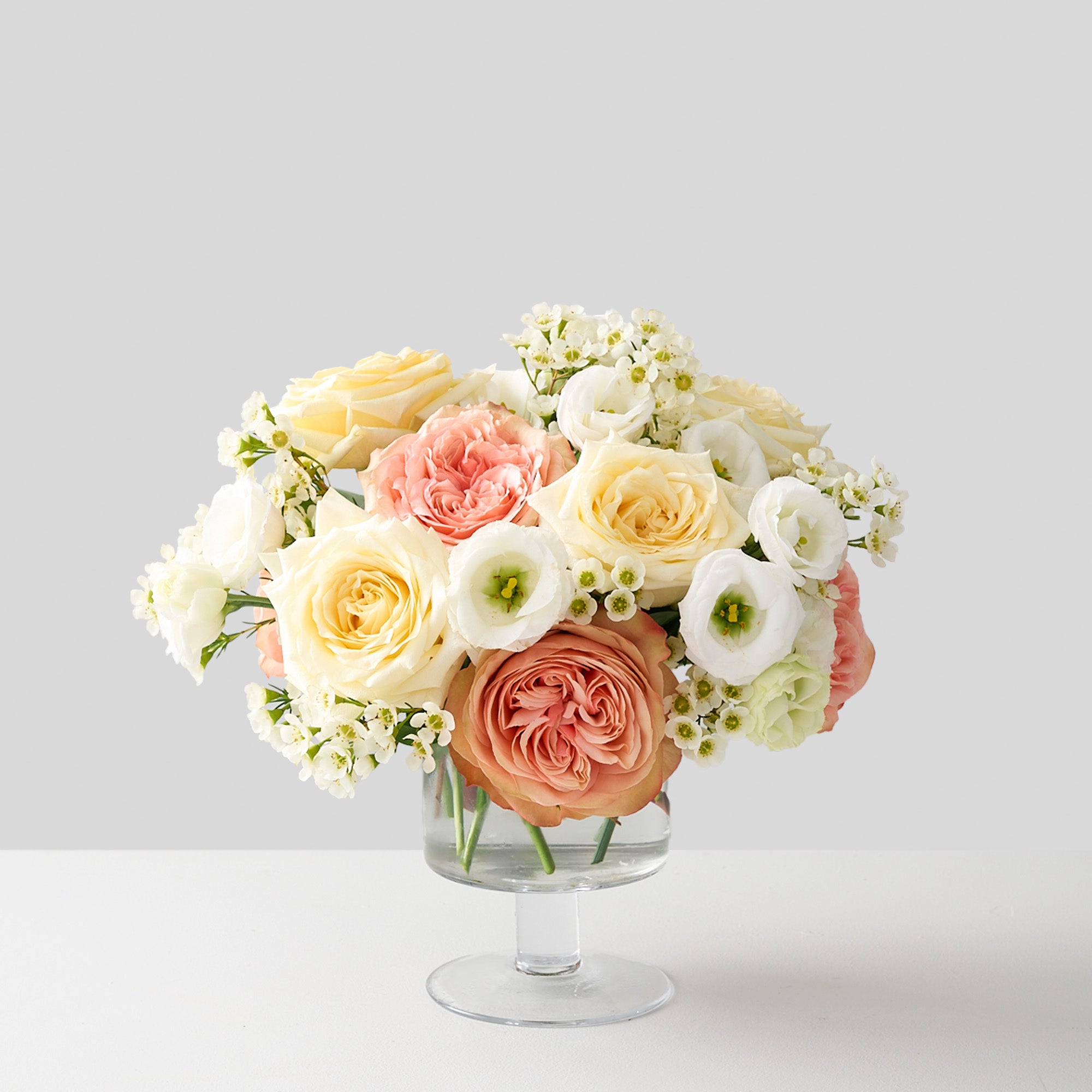 pink khala  and creamy  white candlelight roses, white wax flowers and lisanthus in a pedestal glass vase.