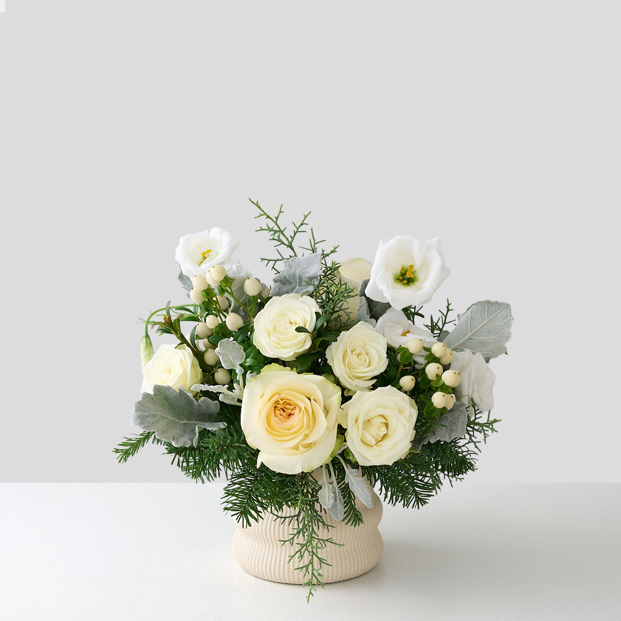 Arrangement of white roses, lisianthus, hypericum, dusty miller leaves and fur tree and cedar leaves.