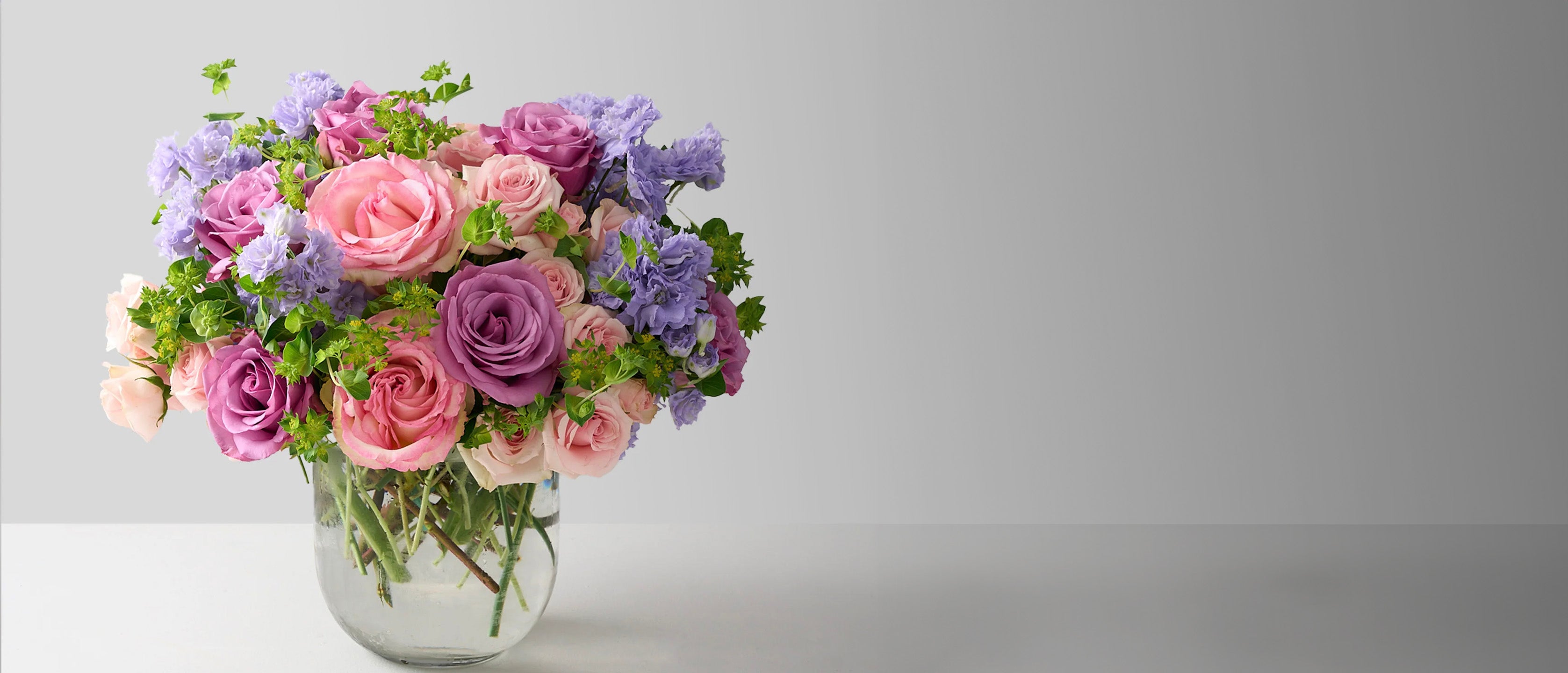 Bouquet of pink, purple, and green flowers in a clear vase on a gray background