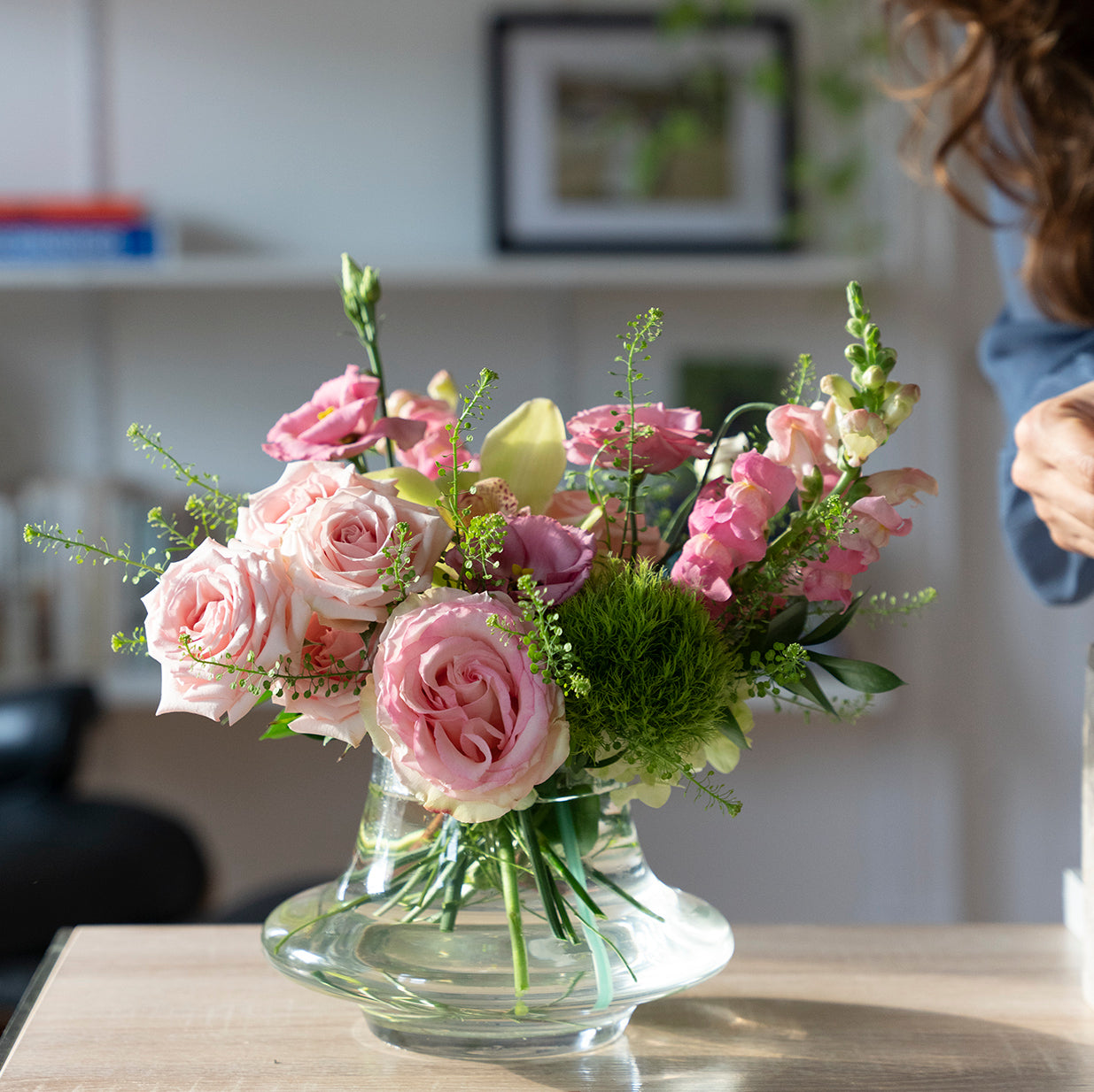 arrangement with pink roses, green trick mums, snap dragons in a clear glass genie vase in a living room