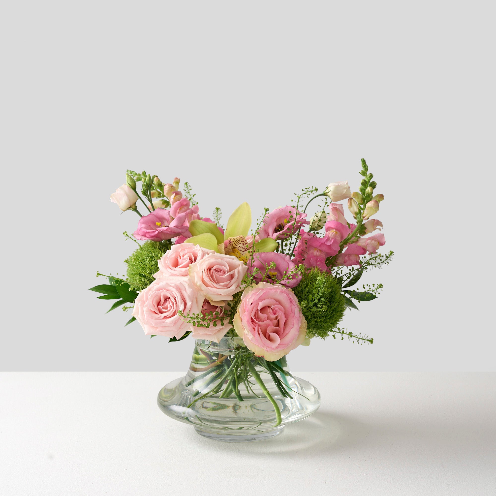 gabrielle arrangement with pink roses, green trick mums, snap dragons in a clear glass genie vase 