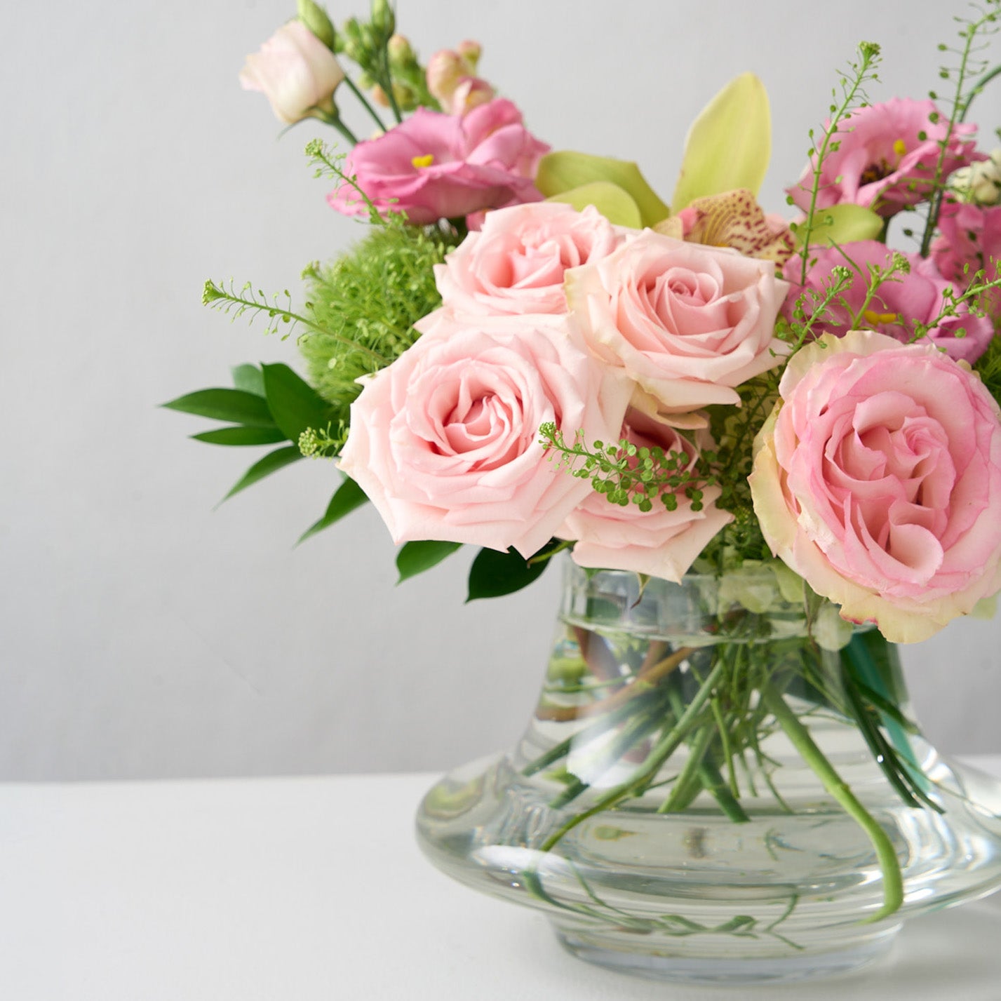 arrangement with pink roses, green trick mums, snap dragons in a low glass genie vase 