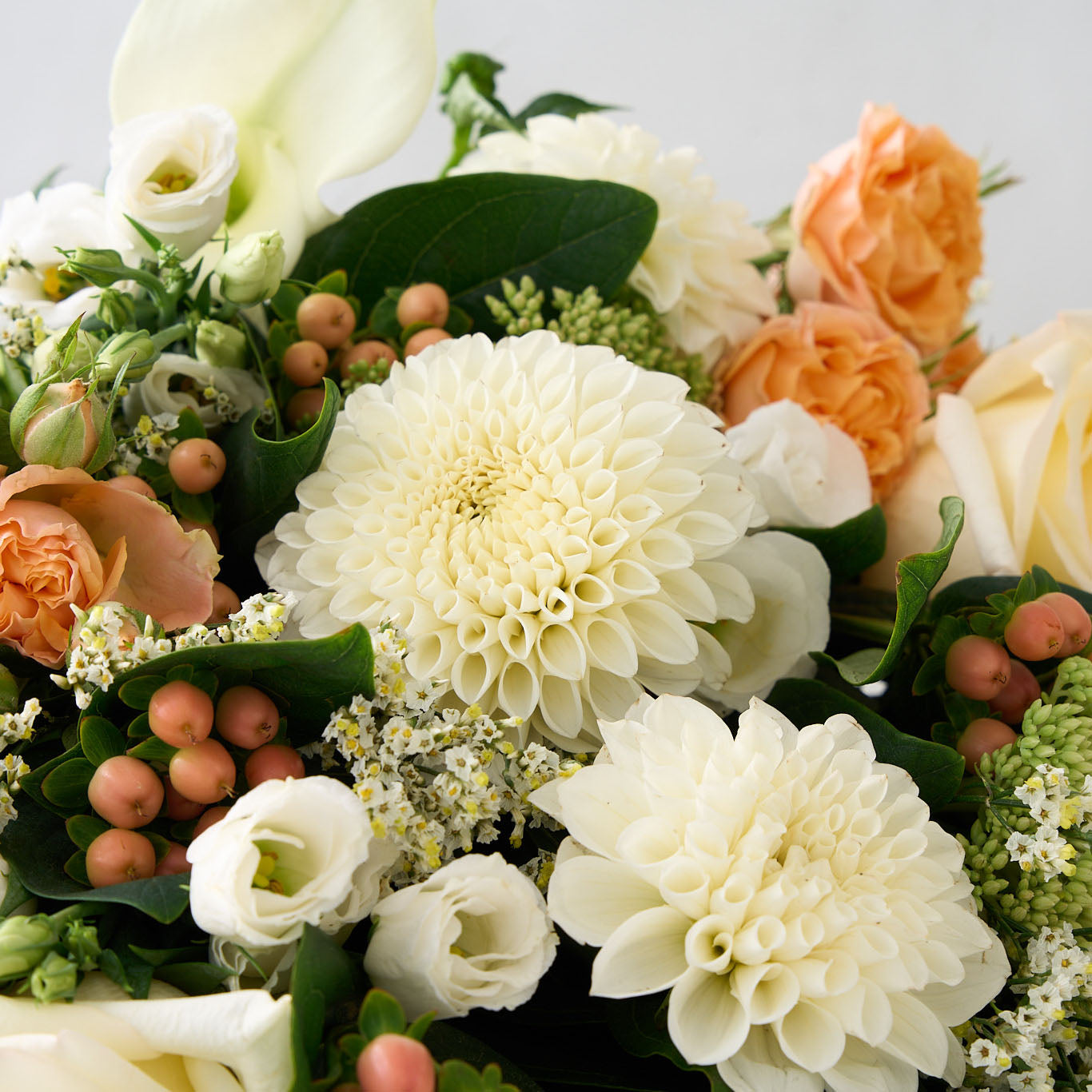 Bouquet of white pompom dahlias and Lisianthus, peach hypericum and rose with greens  on a light background