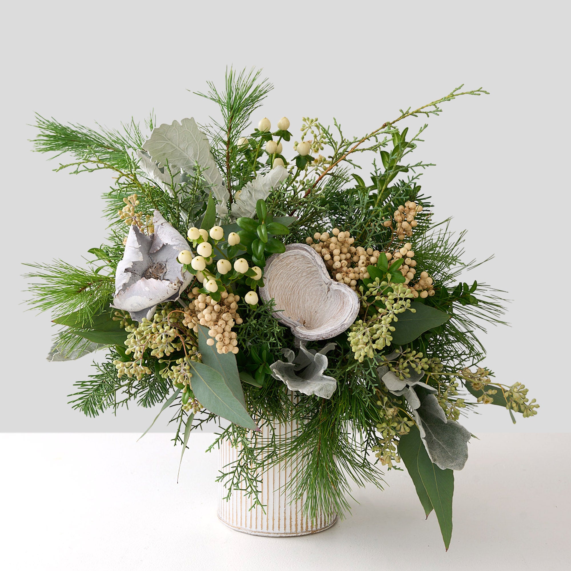 White Pine, cedar, seeded eucalyptus, white hypericum, boxwood in a white deco pot with silver accents.