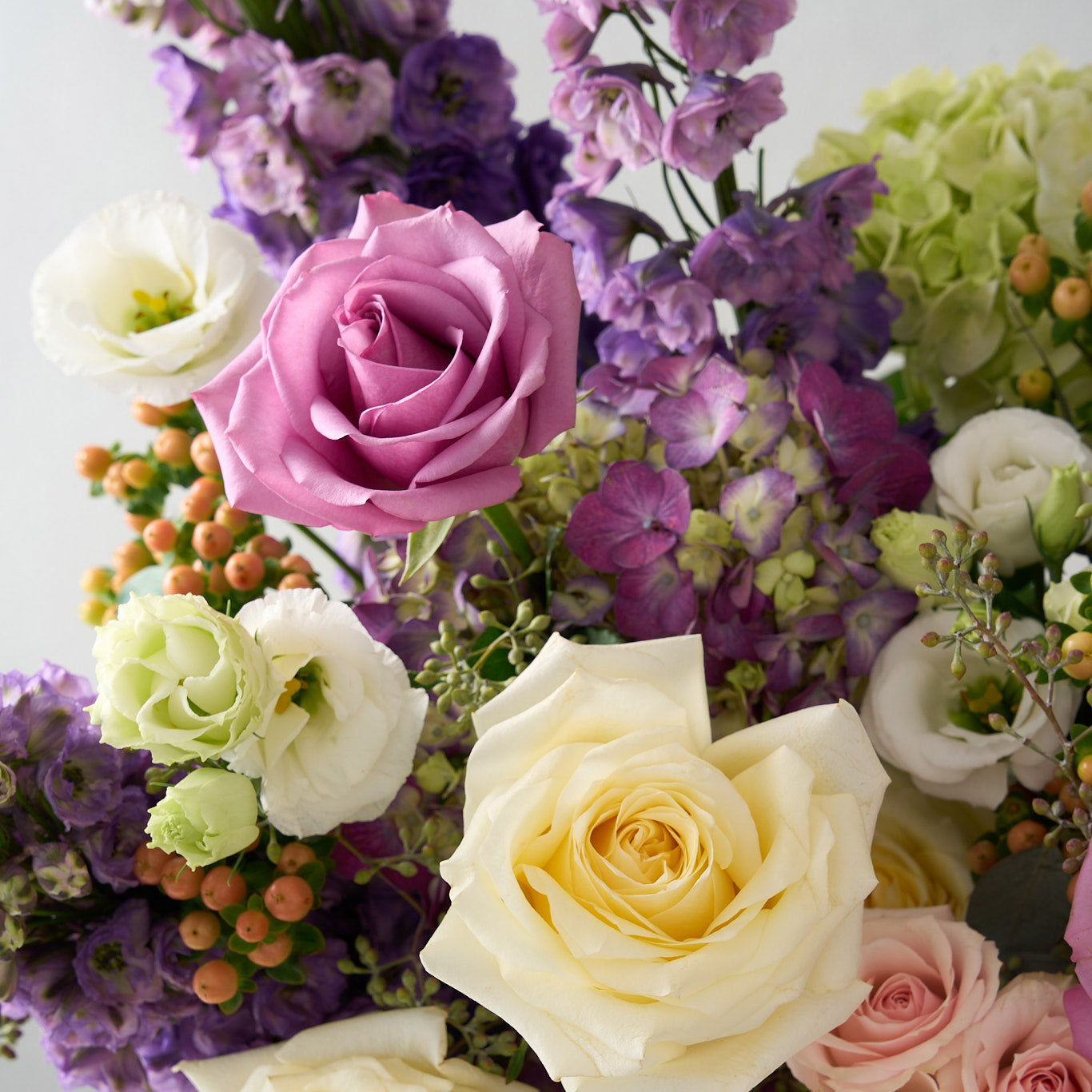 up close photo of mauve piacere and white candlelight rose with purple delphinium, hydrangea and white lisianthus and peach hypericum