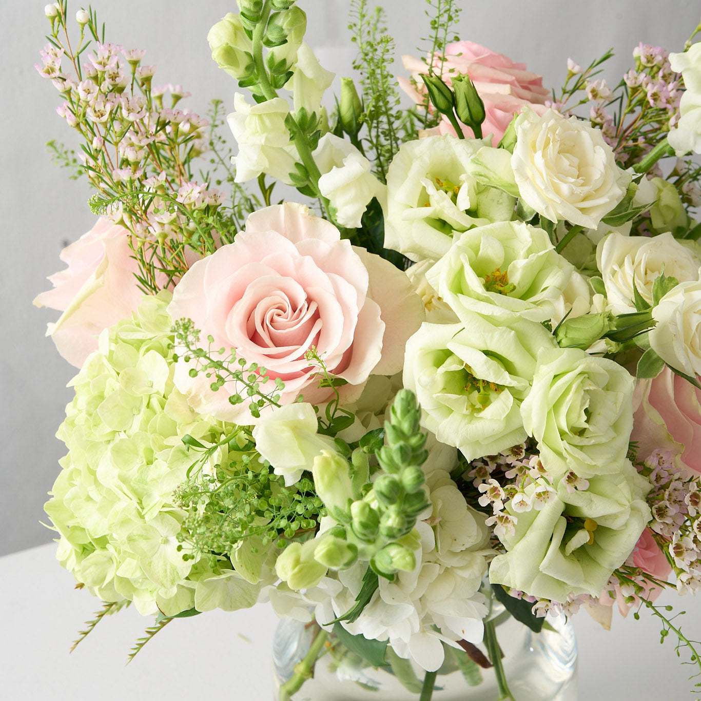 photo of a traditional colours scheme arrangement adorned with pink oses, white lisianthus, tall snap dragons and wispy  green hydrangea