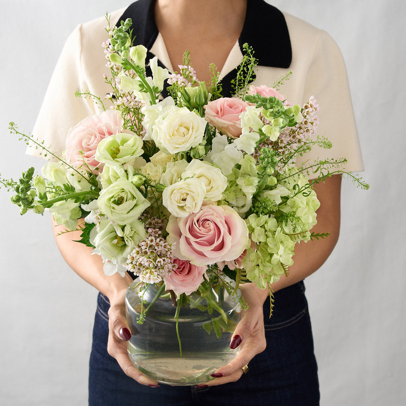 woman holding a traditional colours scheme arrangement adorned with pink oses, white lisianthus, tall snap dragons and wispy  green hydrangea