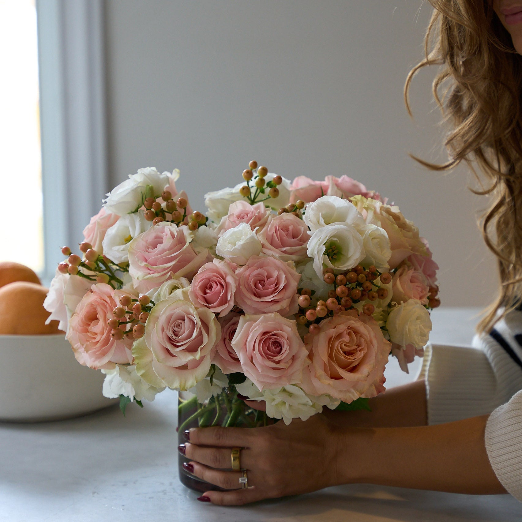 Woman placing medium pink and white floral arrangement on a table