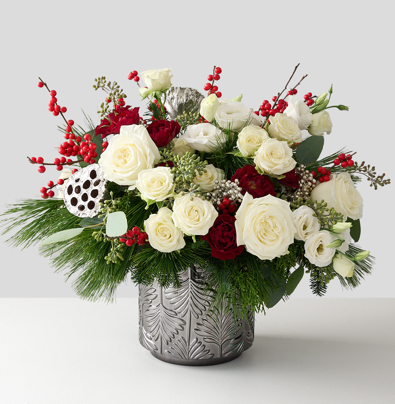 floral arrangement with silver lotus pods, red ilex berries, silver peppercorn  berries, winter greens in a silver tin vase