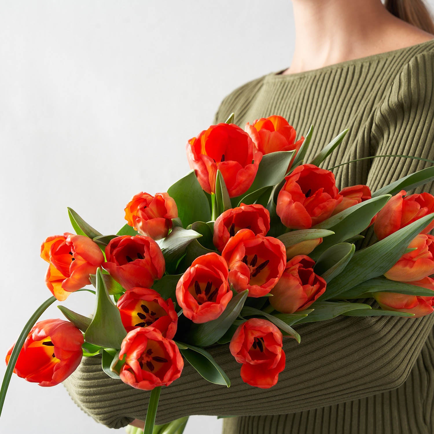 Woman in green sweater holding a large orange tulip bouquet