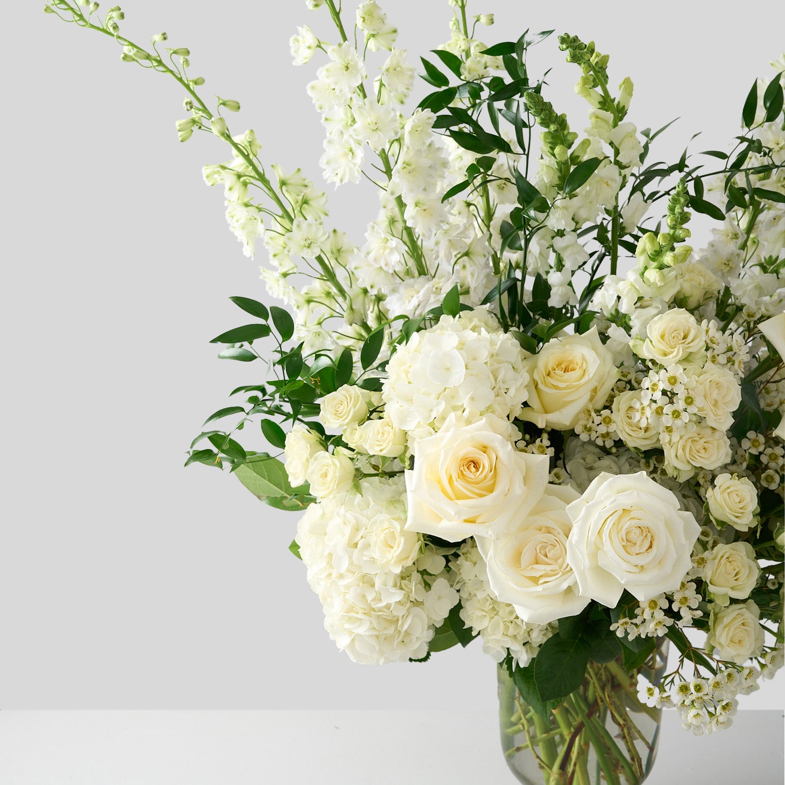 photo of an arrangement  with Candlelight roses, white delphiniums and hydrangeas with whimsical Italian ruscus. 