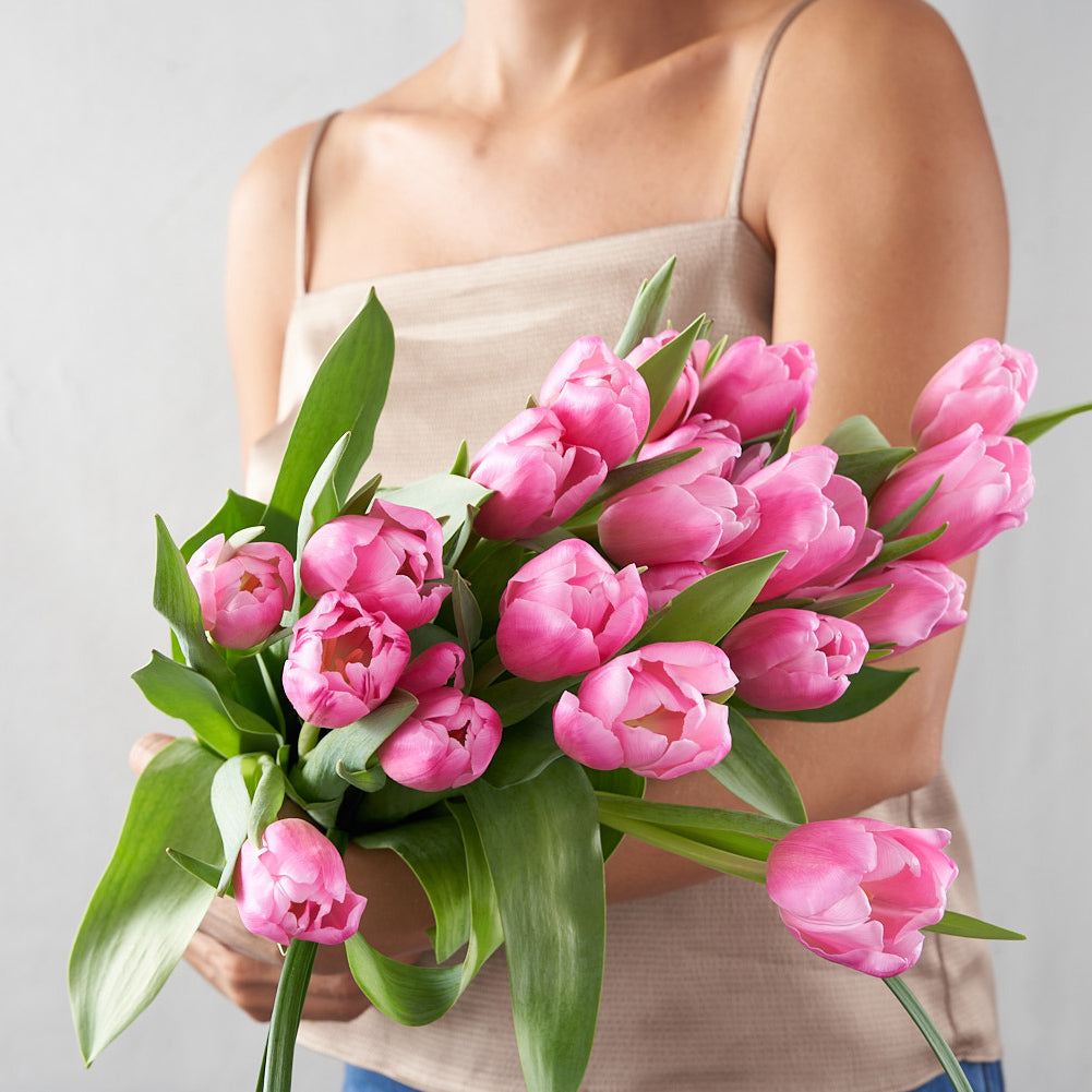 Woman in beige  top holding an bouquet of pink tulips in her arms