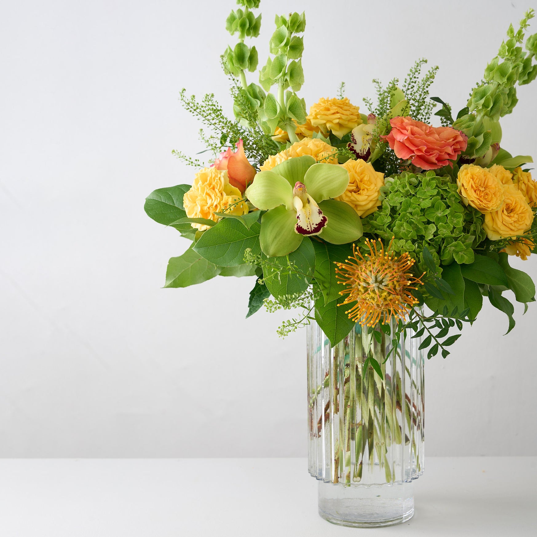 Bouquet of yellow, orange and green flowers in a clear vase on a light gray background