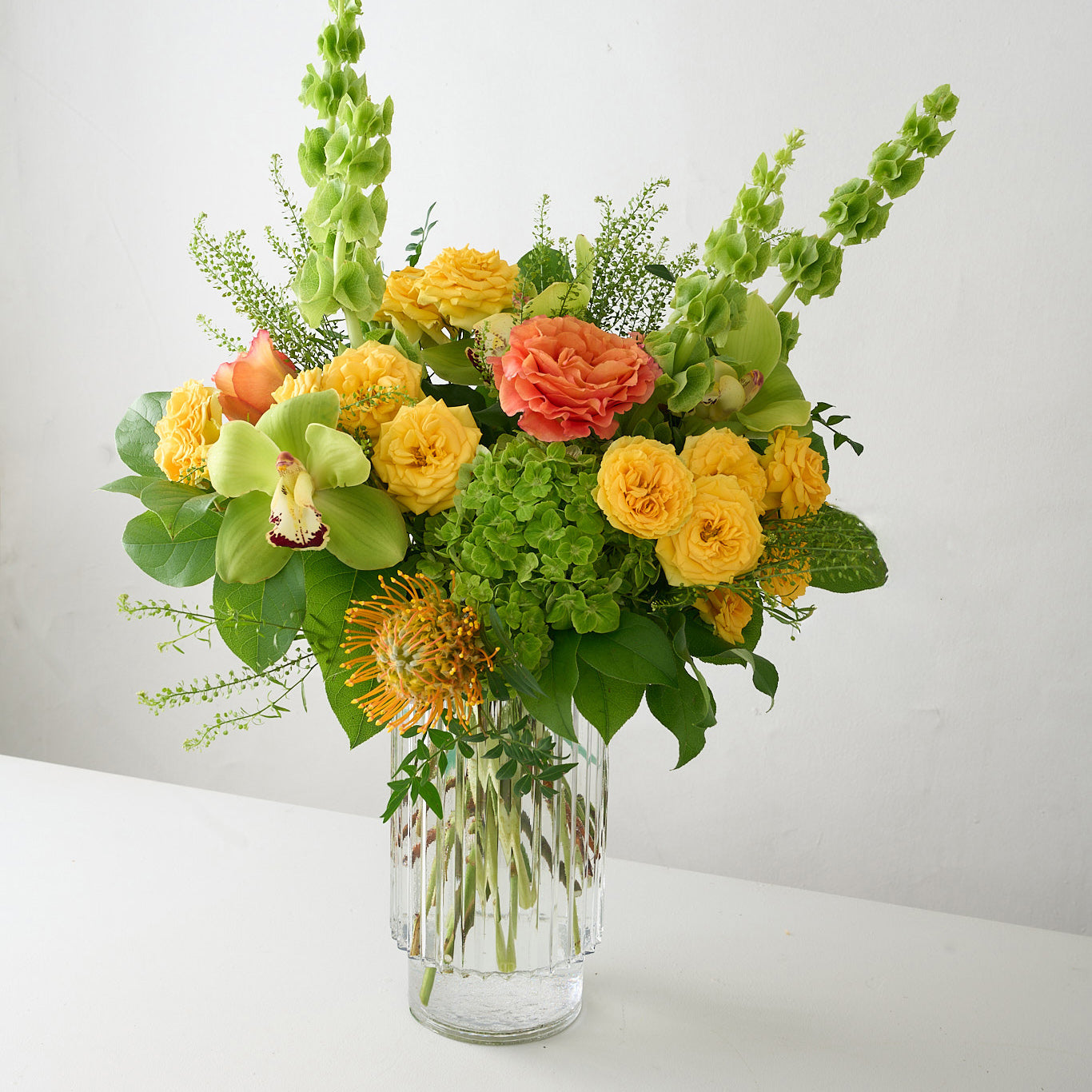 Bouquet of yellow, orange and green flowers in a clear vase on a light gray background