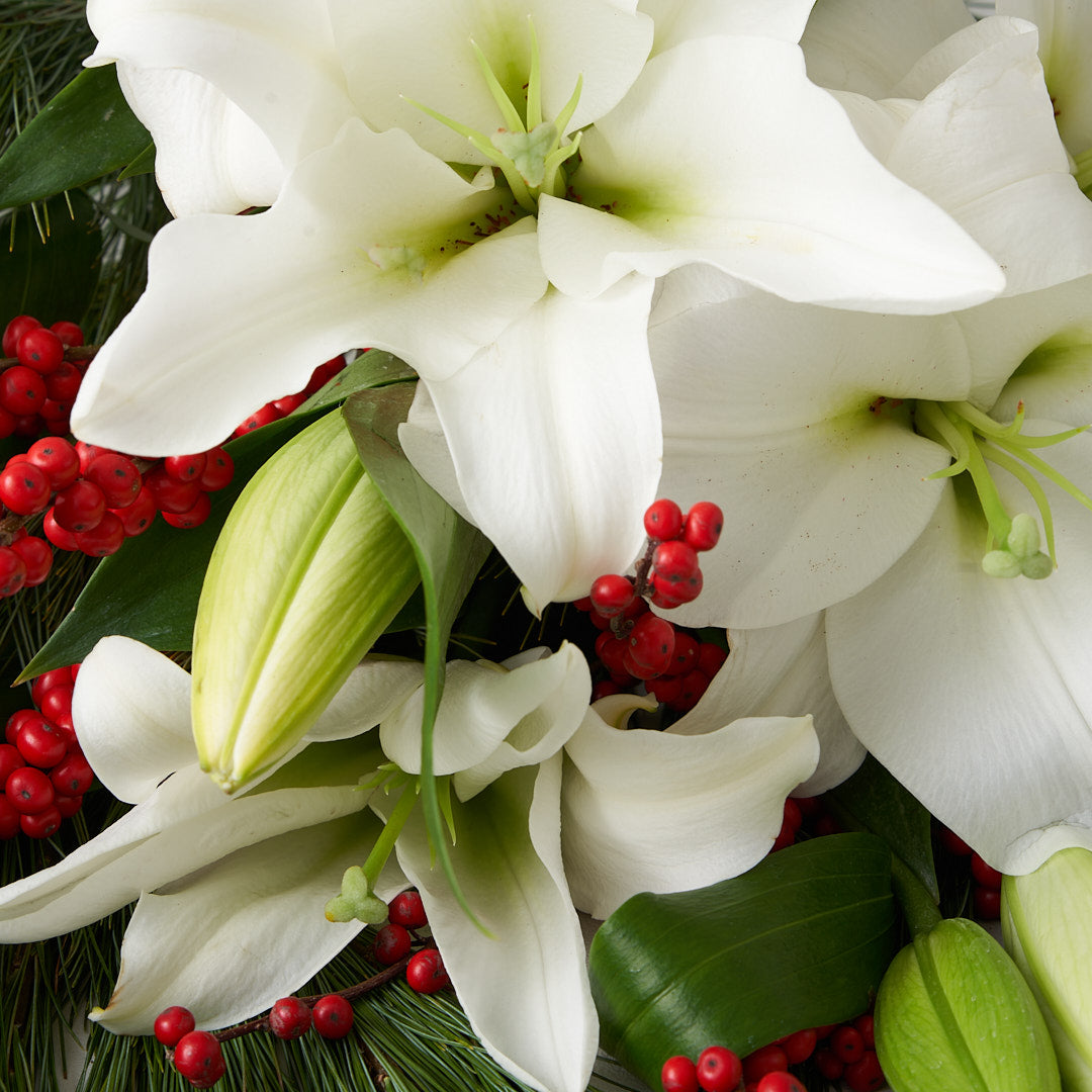 Closeup of white lilies, red berries, and pine.