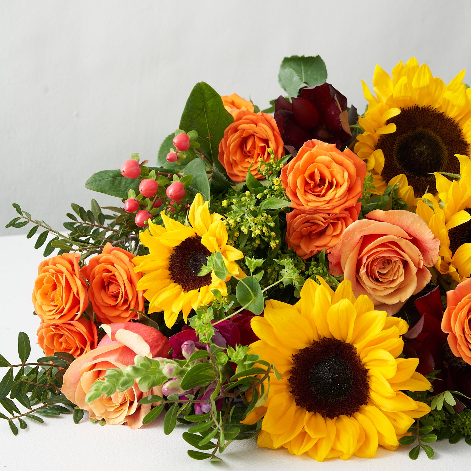 Bouquet of summer flowers including sunflowers, free spirit roses, kahala roses, red hypericum berries, and more plus greenery