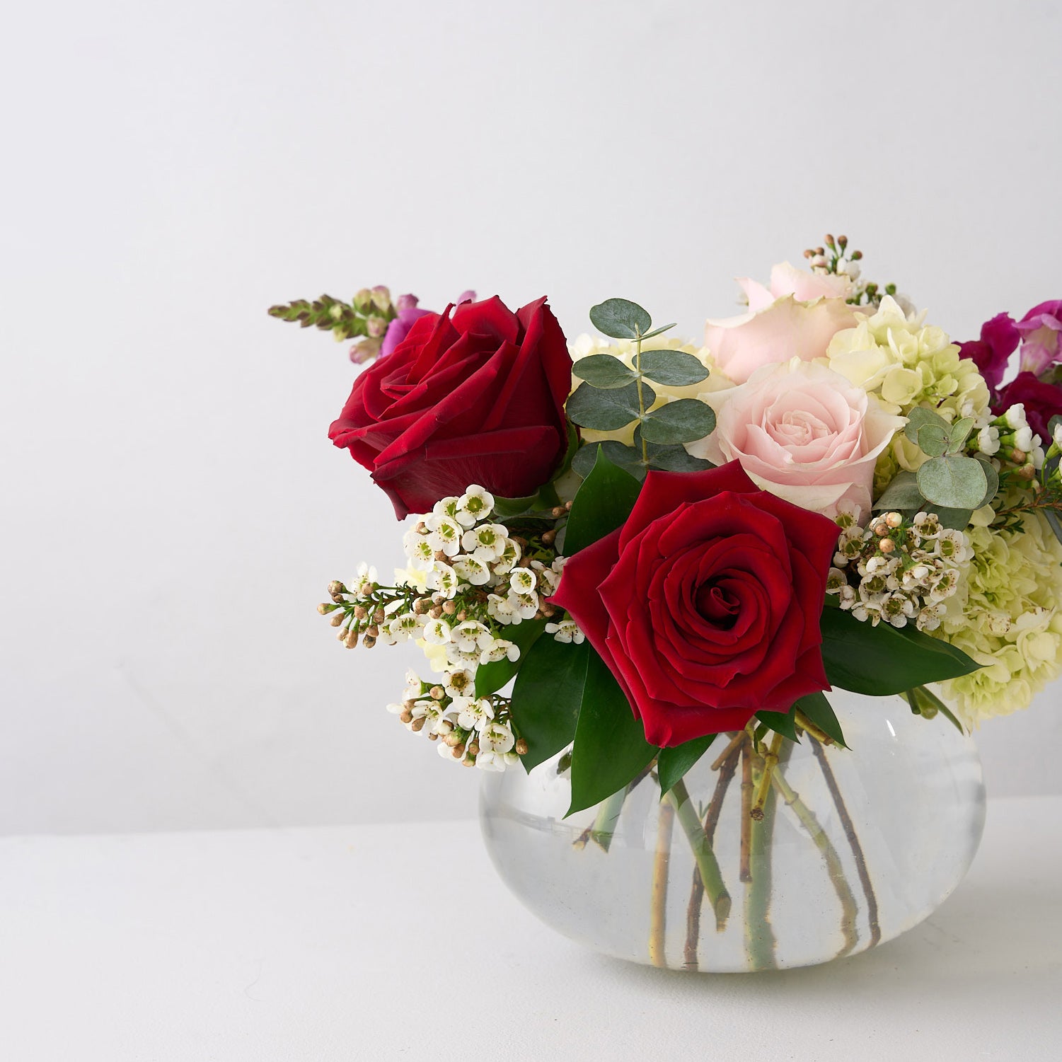 Valentine's day arrangement of deep red, & soft pink roses with hot pink  snapdragons in a small round, clear vase.
