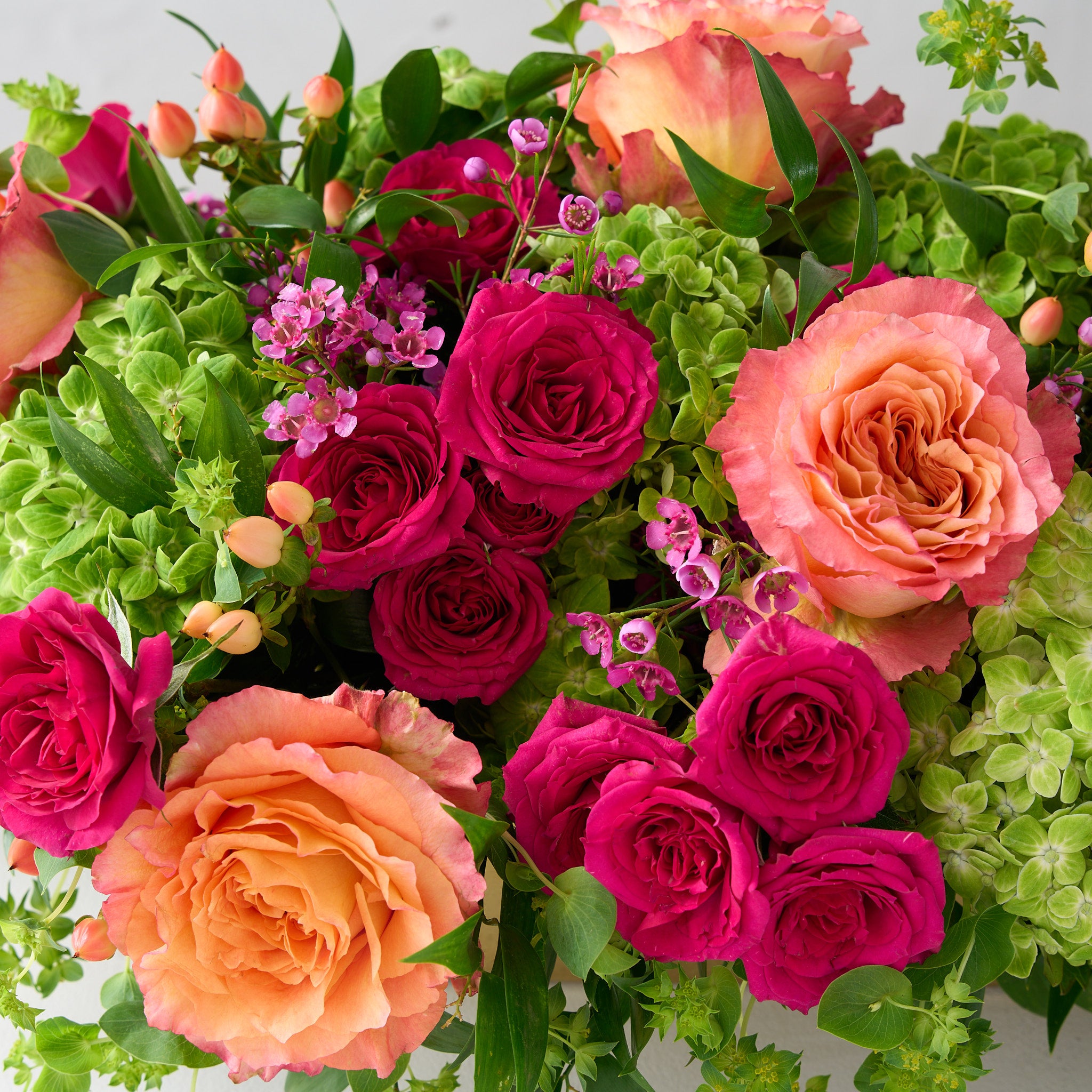 up close picture of of green hydrangea, coral free spirit roses, pink wax flowers and fuchsia spray roses.