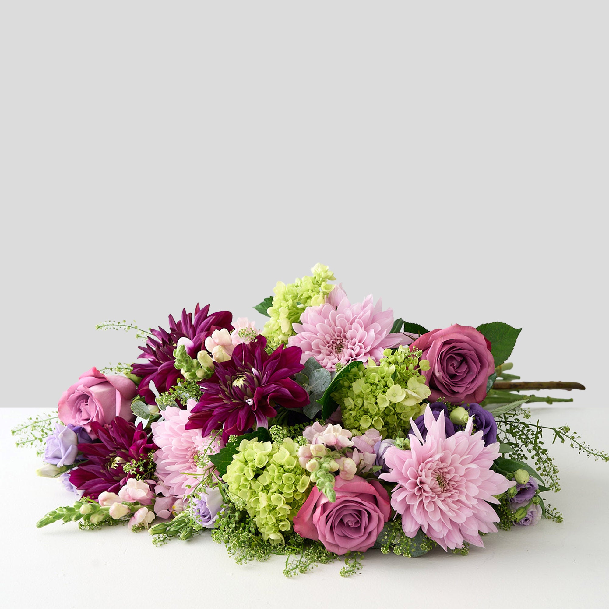 Bouquet of purple, pink dahlias, mauve long stemmed roses green  hydrangea and lavender Lisianthus on a light gray background