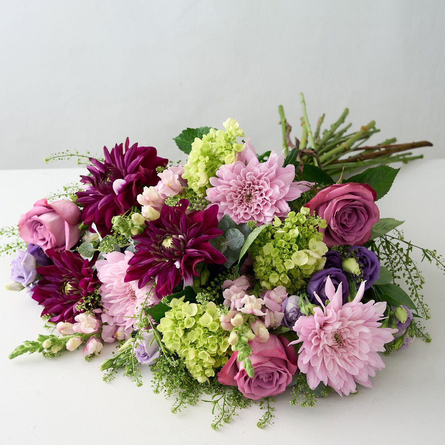 Bouquet of purple, pink dahlias, mauve long stemmed roses green  hydrangea and lavender Lisianthus on a light gray background