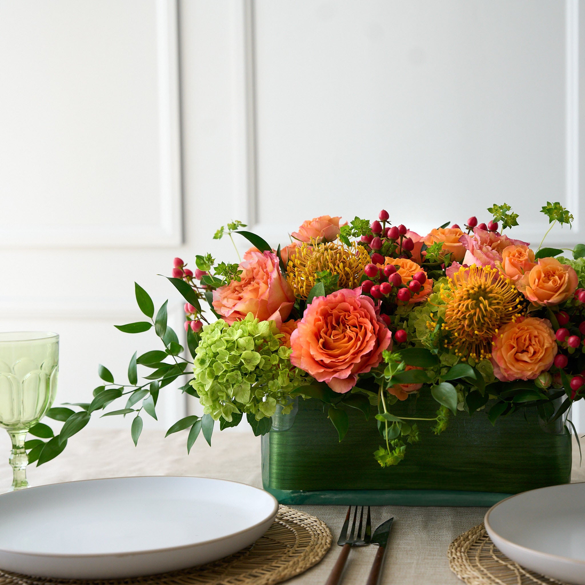 rectangle dinner table center piece  lined with green leaves, with coral roses and hiypericum, green hydrangea on a dinner table