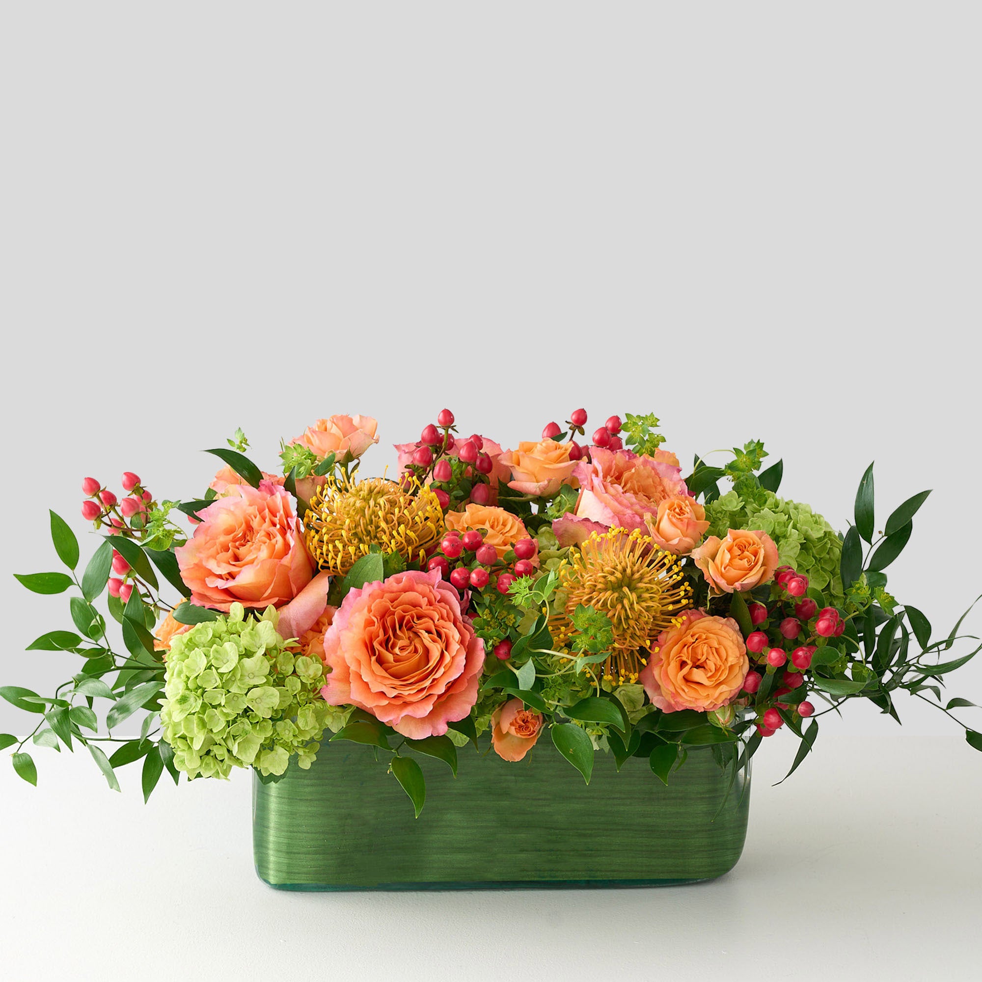 rectangle dinner table center piece  lined with green leaves, with coral roses and hiypericum, green hydrangea 