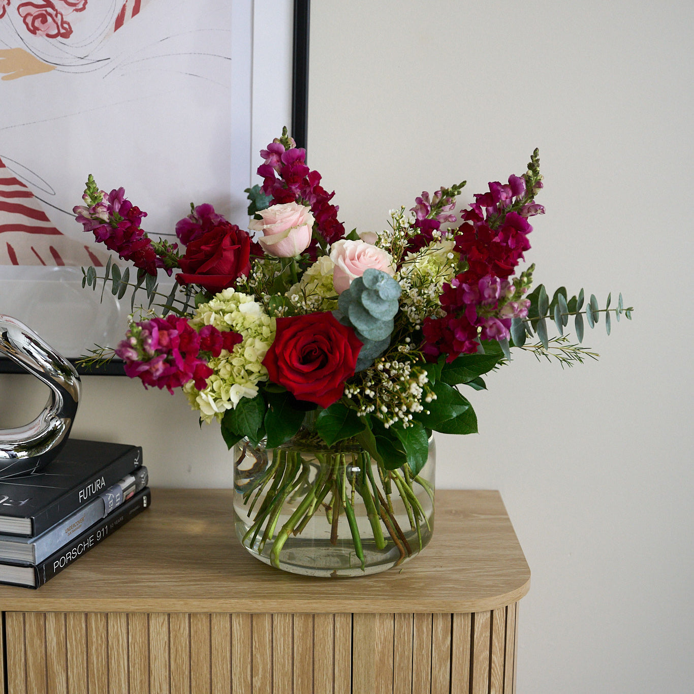 Valentine's day arrangement with hot pink snapdragons, soft pink  and deep red roses in a large clear vase on a wooden credenza