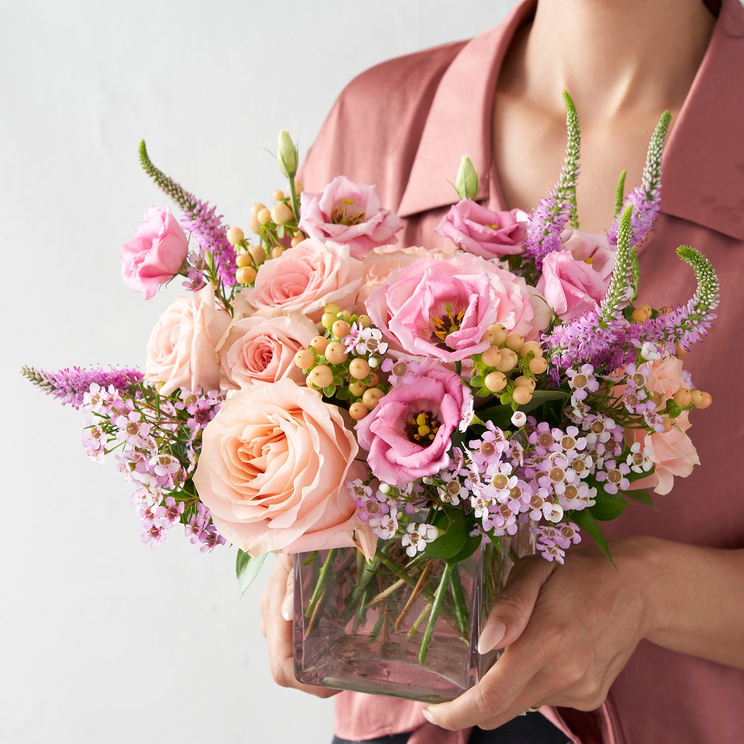 Woman in pink shirt holding pink and peachy pink flower arrangemnt.