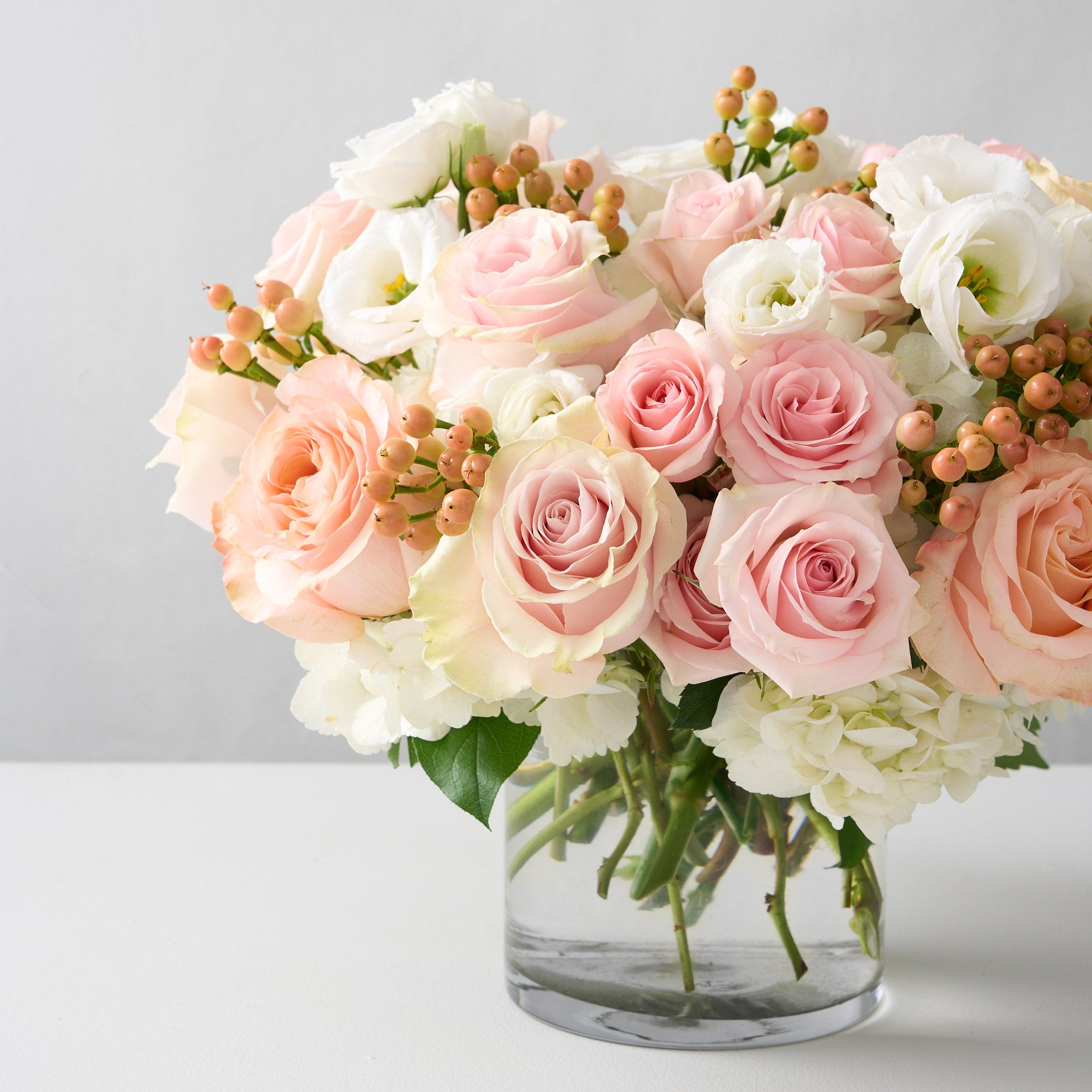 Sophie arrangement up close , peach and pink roses with peach hypericum in a clear glass cylinder vase