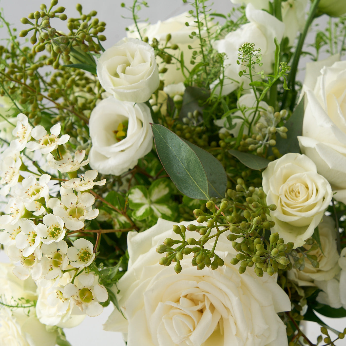 up close photo of flowers in an elegant all white and green country garden vase arrangement which features hydrangea, snapdragons, Playa Blanca roses, lisianthus, seeded eucalyptus, and white spray roses.