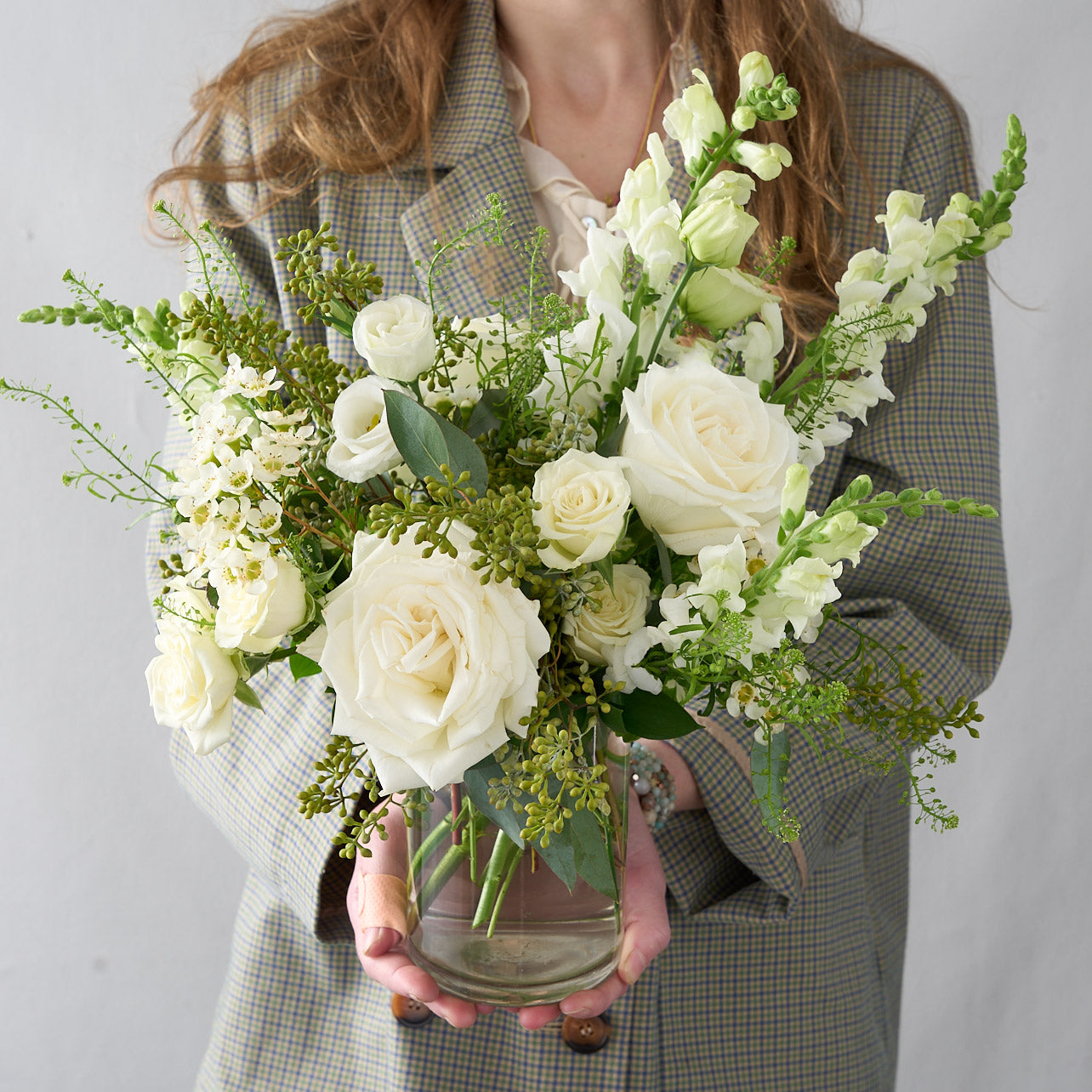 elegant all white and green country woman holding a garden vase arrangement which features hydrangea, snapdragons, Playa Blanca roses, lisianthus, seeded eucalyptus, and white spray roses.