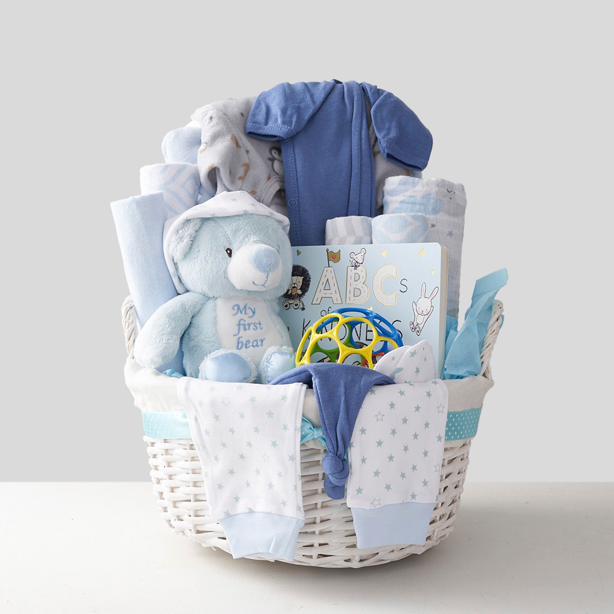 Blue baby basket for newborn with teddy bear, toys, books, clothes, shoes and pajamas.