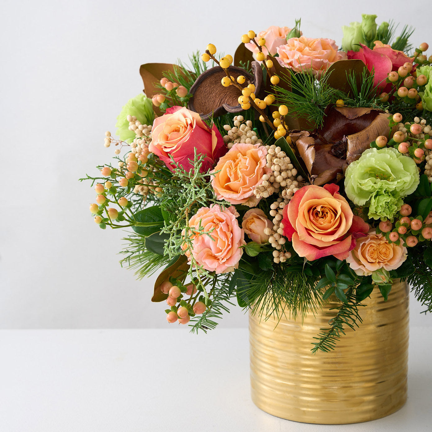 large arrangement of peach roses, hypericum, green double Lisianthus, magnolia leaves, cedar, palm pods and white pine in a gold tin pot.