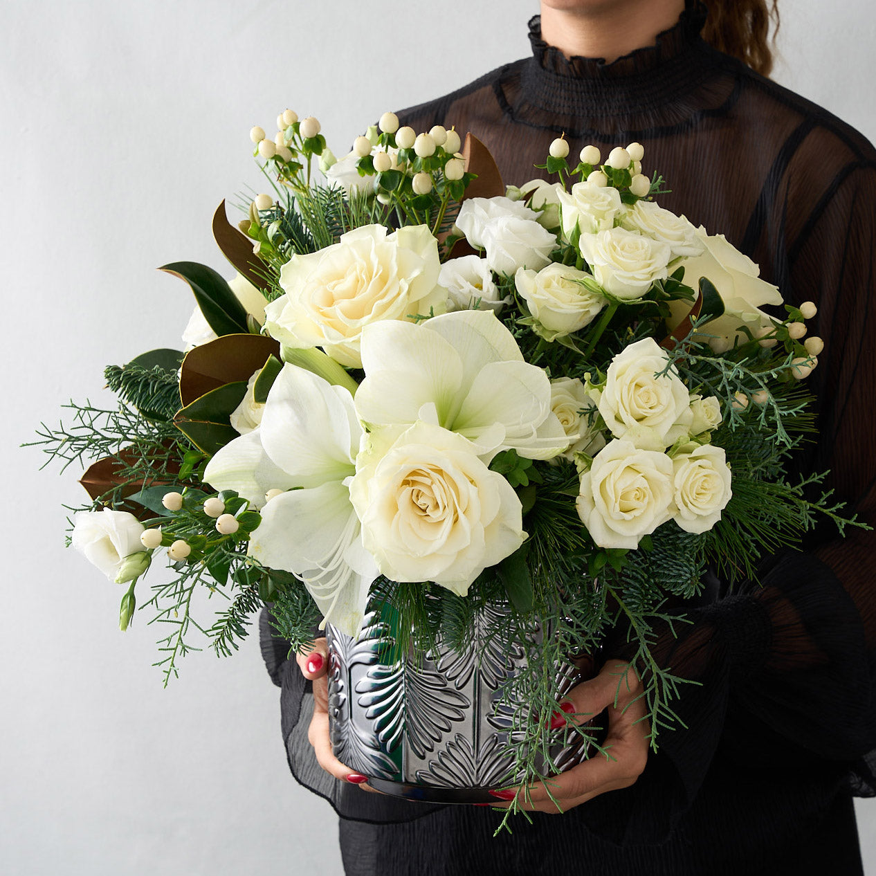 picture of woman in black blose holding a christmas arrangement with white roses, lisianthus, and hypericum with magnolia and winter greens