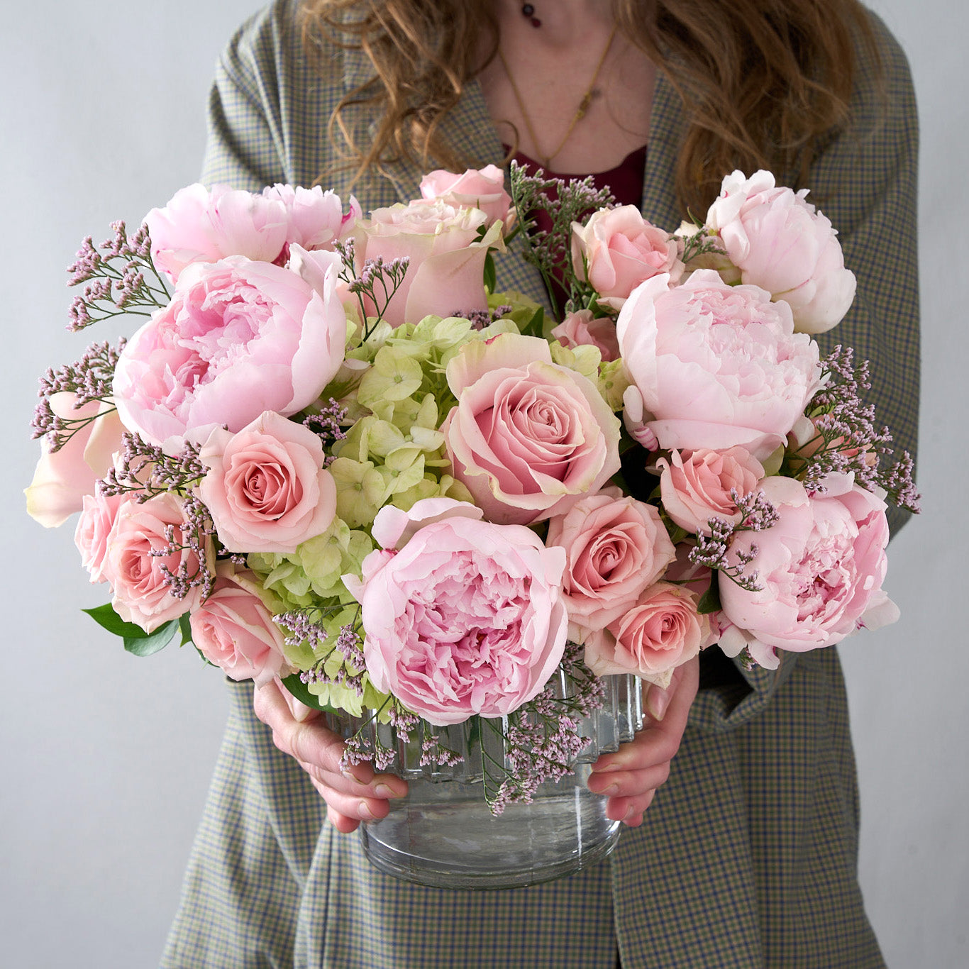 Girl holding glass vase filled with pink peonies, pink roses, baby's breath and green hydrangea