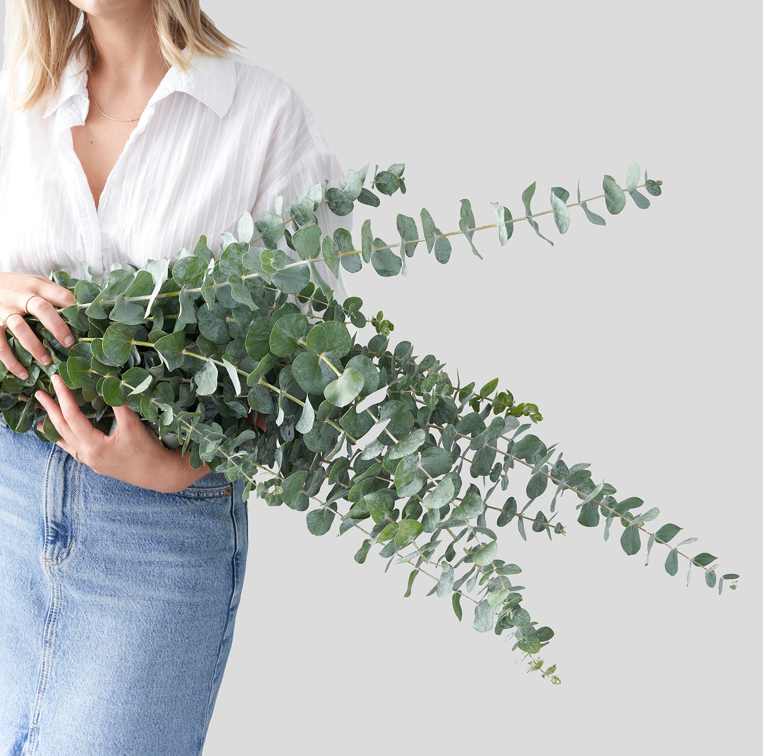 woman in white shirt and jean skirt holding large bouquet of eucalyptus.