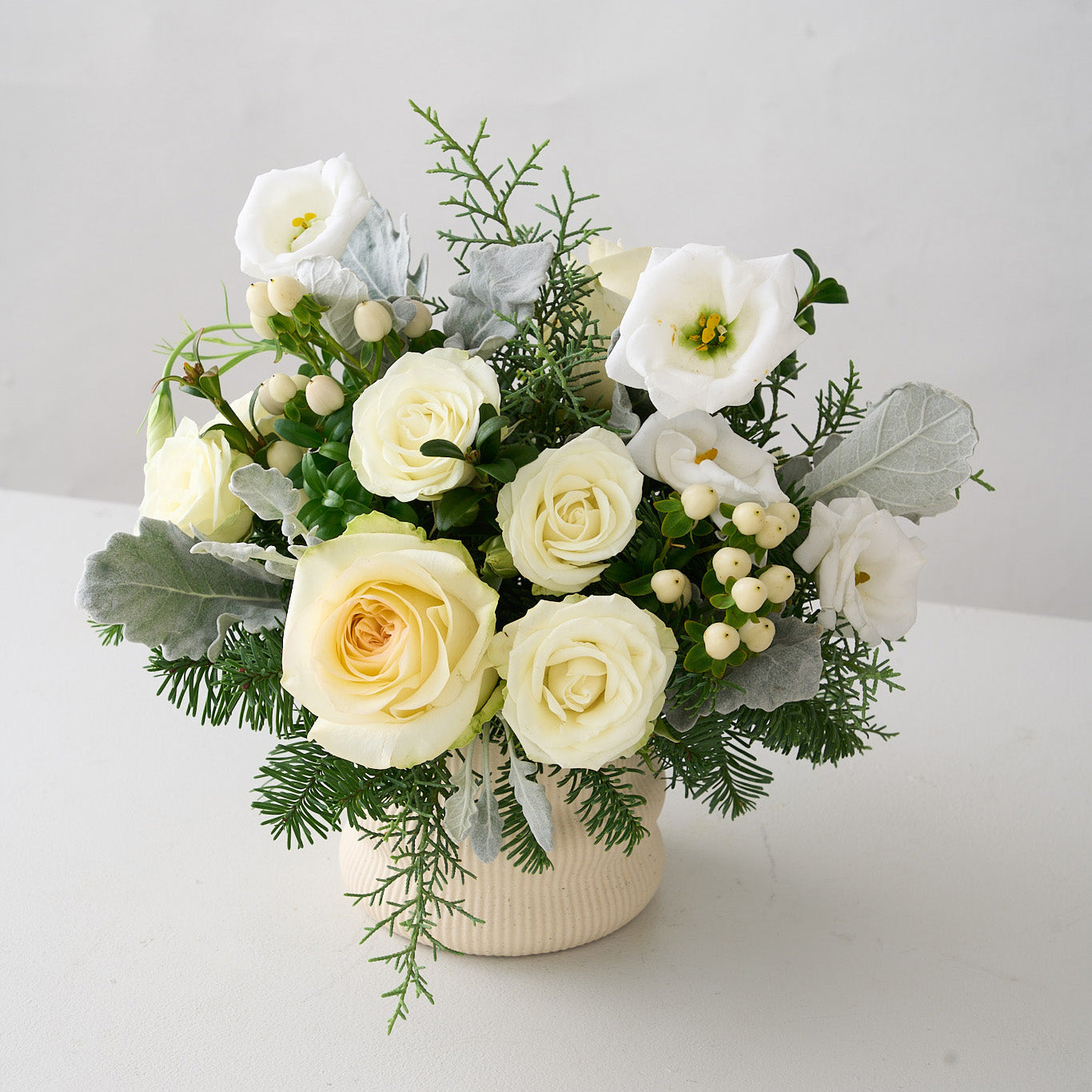 Arrangement of white roses, lisianthus, hypericum, dusty miller leaves and fur tree and cedar leaves.