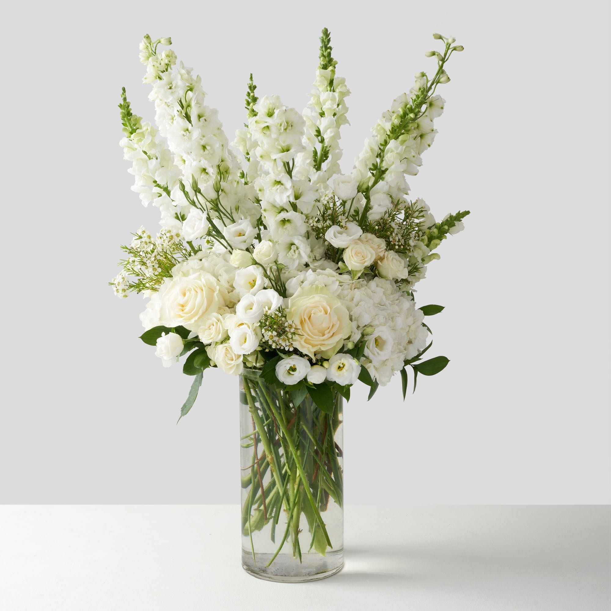 An all white flower arrangement composed of delphinium, roses, lisanthus, wax flower, and hydrangea.
