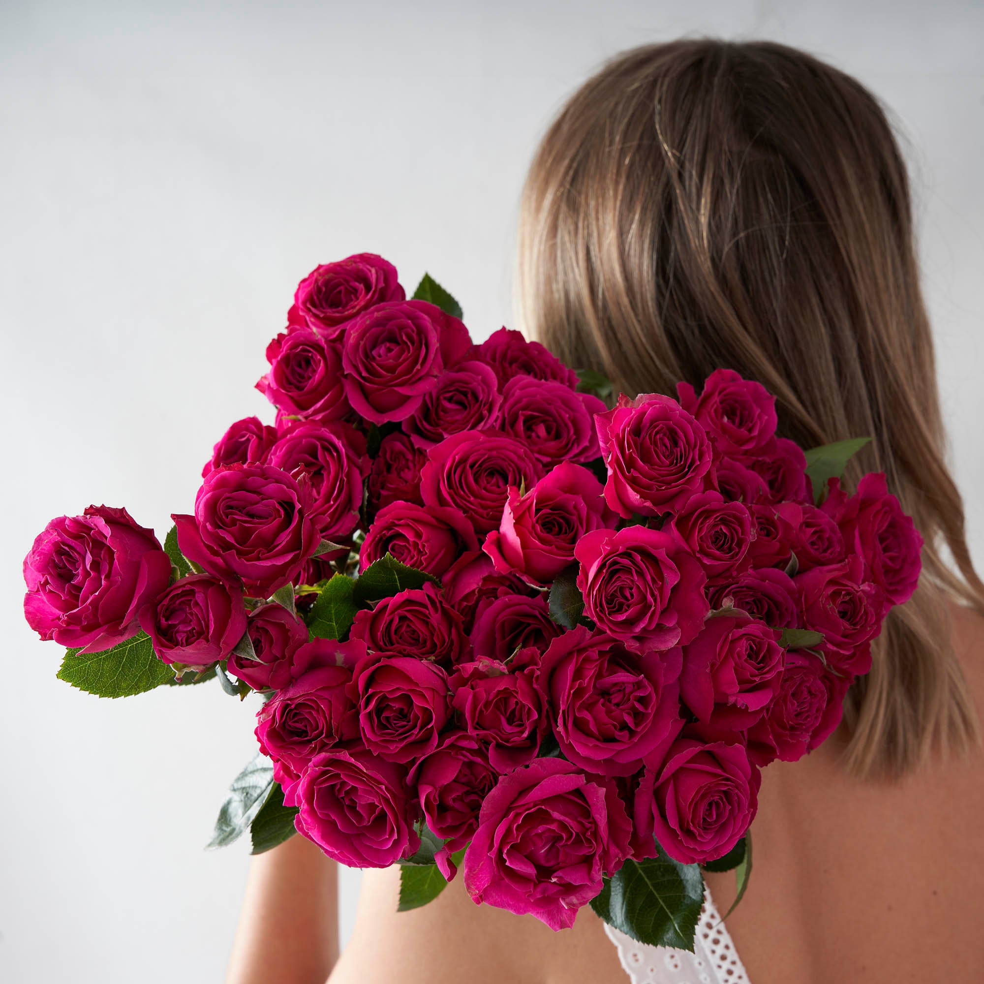 Woman holding bouquet of fuchsia pink spray roses over her shoulder.
