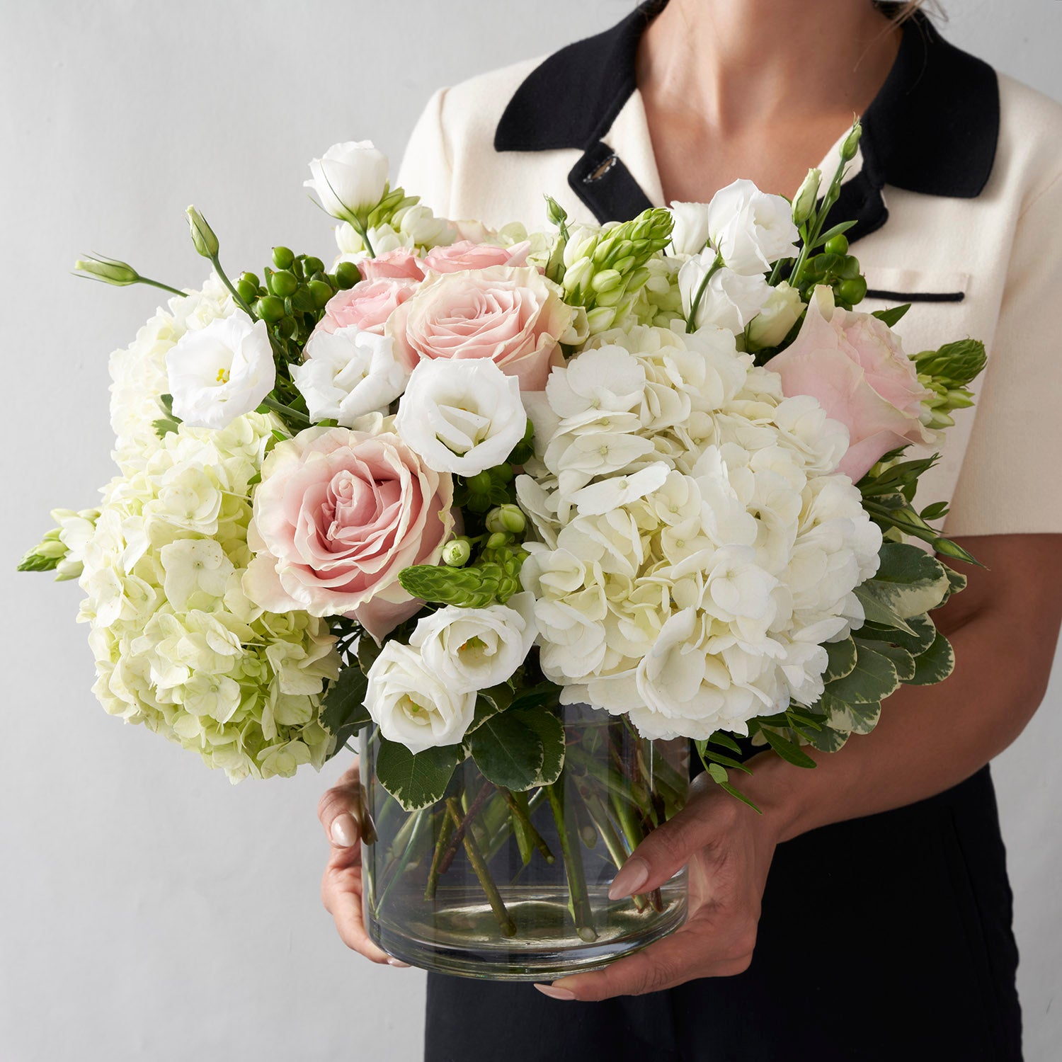 woman wearing black and white, holding large soft pink and white flower arrangement, in glass vase. 