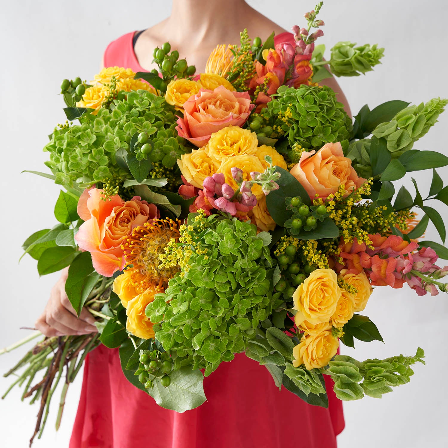 Woman in red dress holding large bouquet of lime green, yellow, and orange flowers.