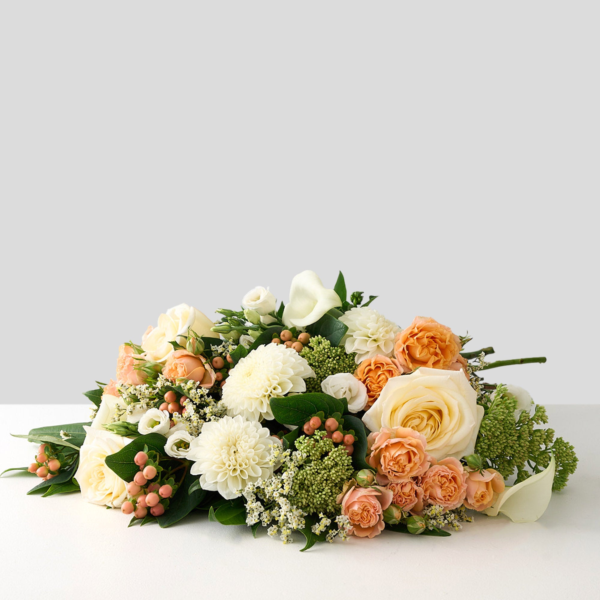 Bouquet of flowers with white dahlias & roses, peach roses and greens on a light gray background