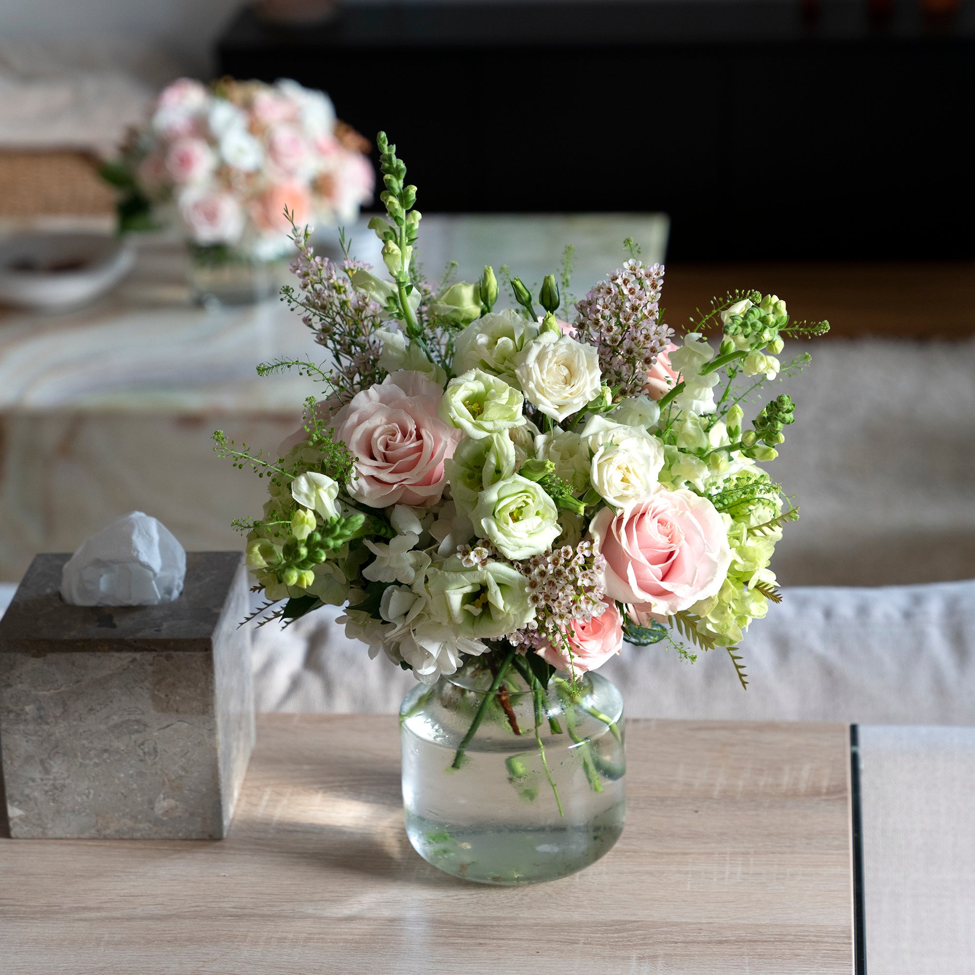 a traditional colours scheme arrangement adorned with pink oses, white lisianthus, tall snap dragons and wispy  green hydrangea in a home setting