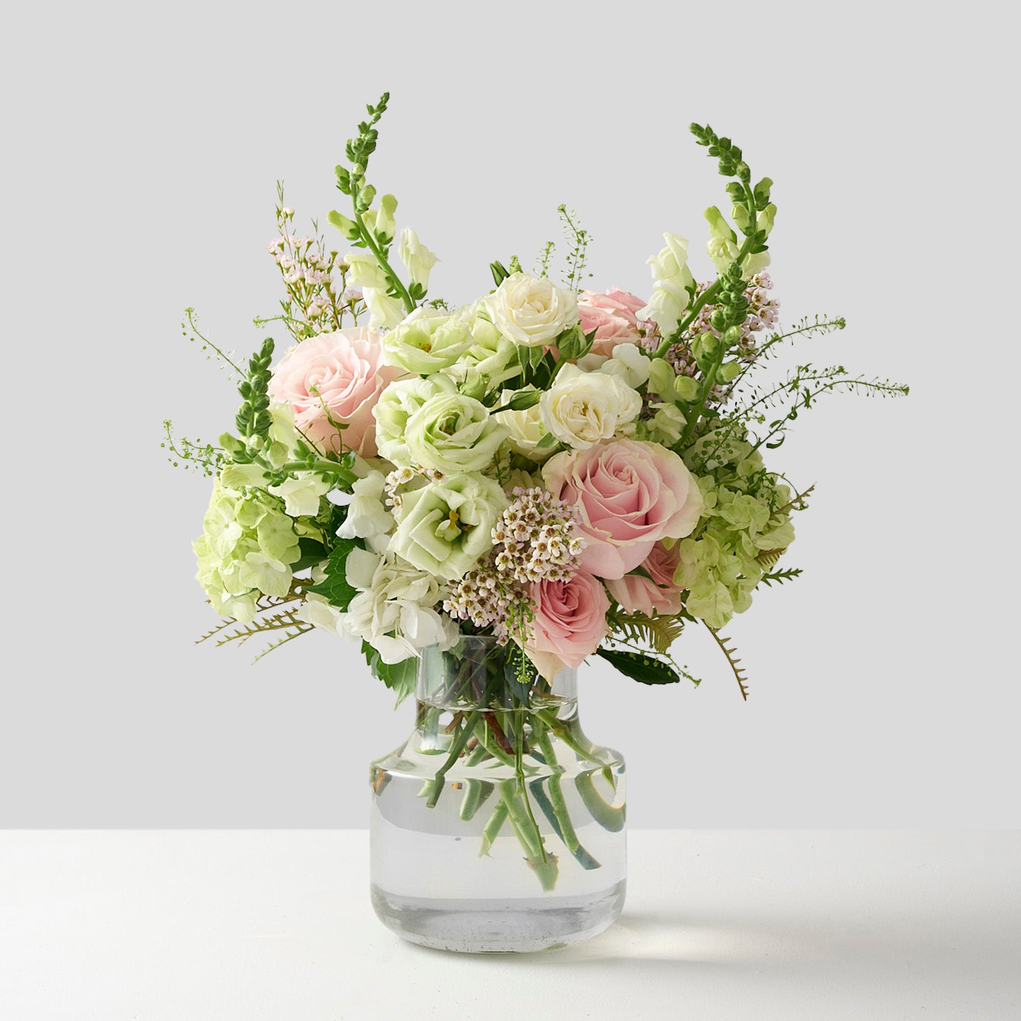 a flower arrangement in a traditional colours scheme adorned with pink roses, white lisianthus tall white snap dragons and wispy hydrangea